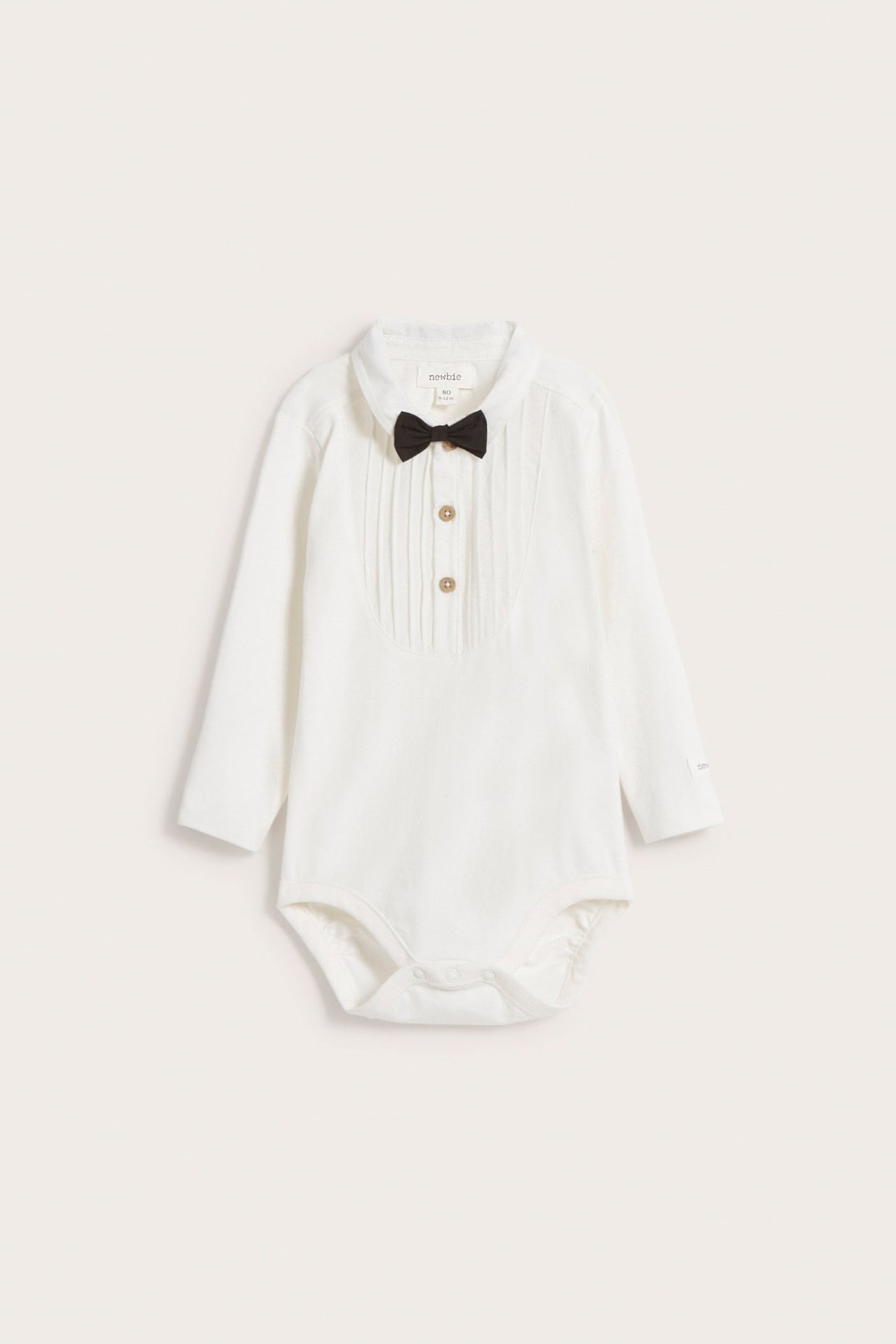 Front view: off-white long-sleeved baby bodysuit with pleated front, buttons, and black bow tie.