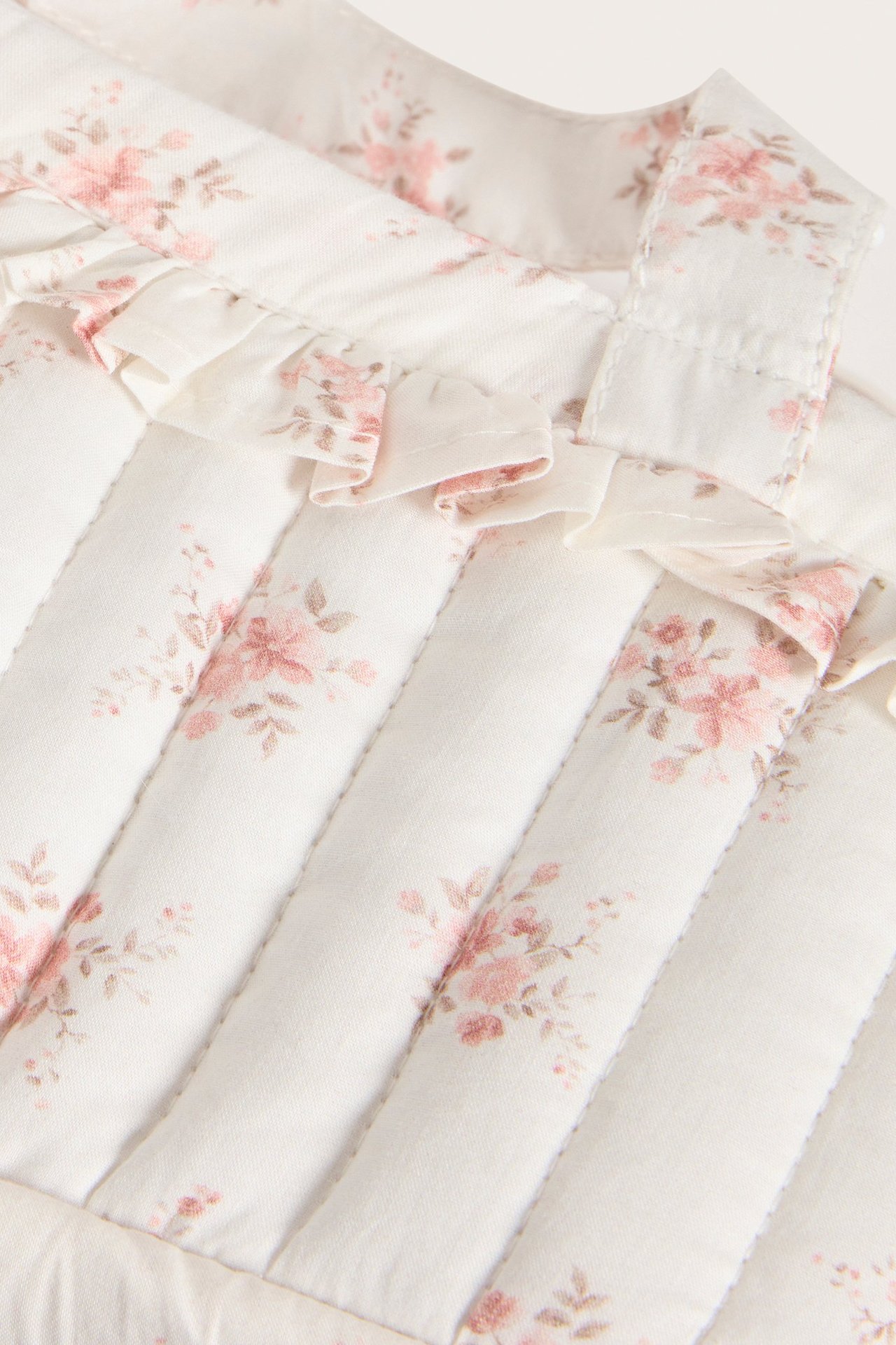 Nahaufnahme eines cremefarbenen, gesteppten Puppenkorbs mit rosa Blumenmuster und Rüschenbesatz.