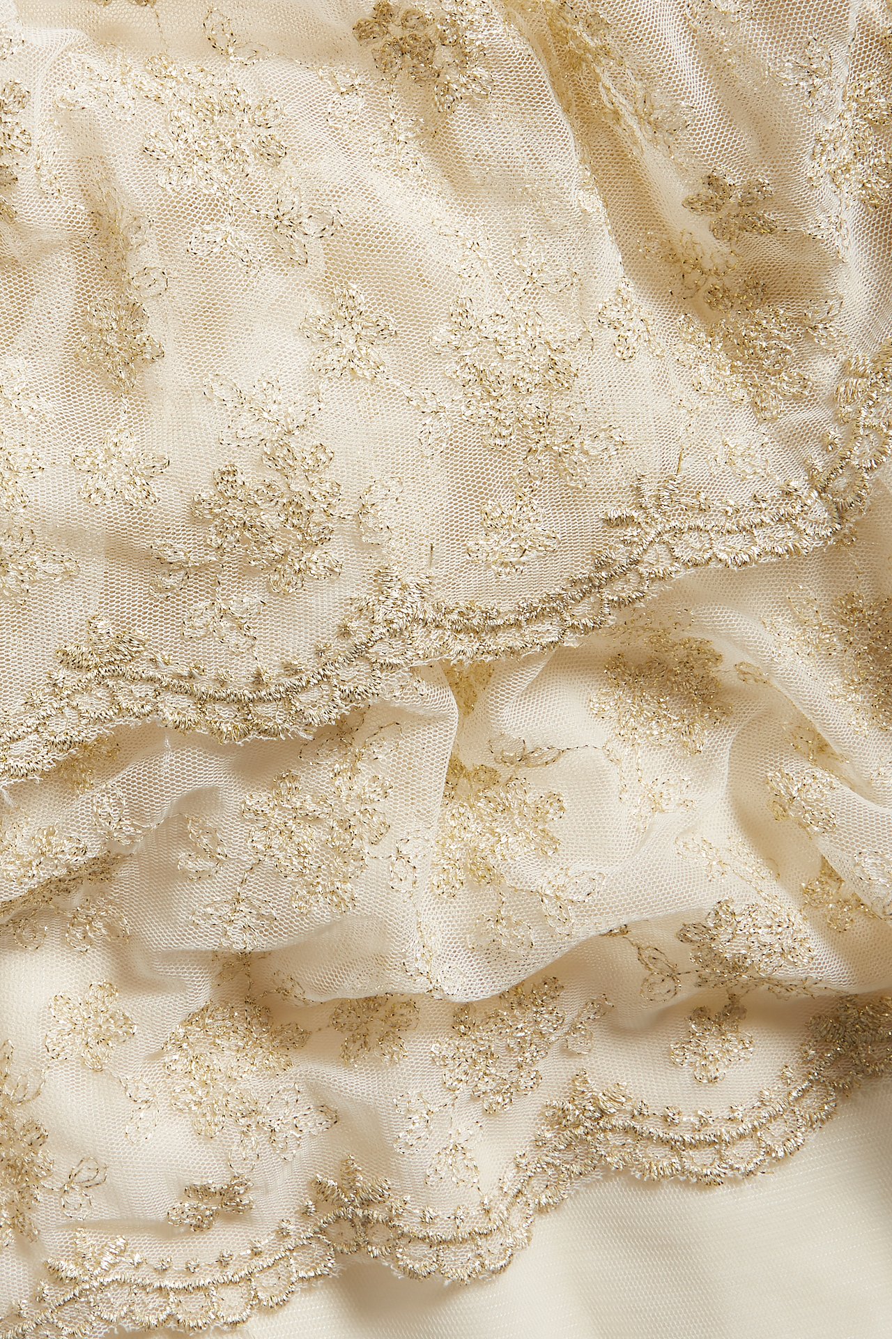 Nahaufnahme von cremefarbenem Mesh-Kleiderstoff mit goldener Blumenstickerei und Wellenkanten.