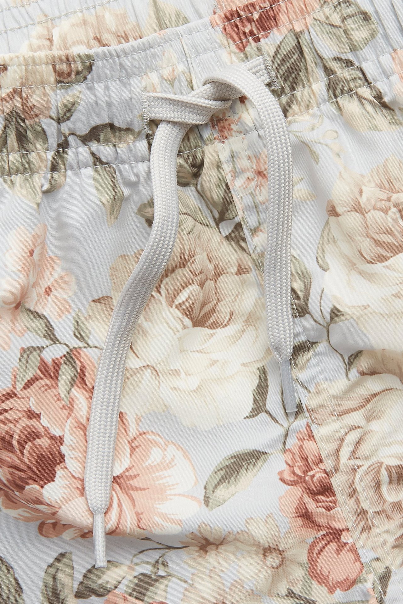 Nahaufnahme von blauen floralen Badeshorts mit elastischem Bund und hellgrauem Kordelzug.