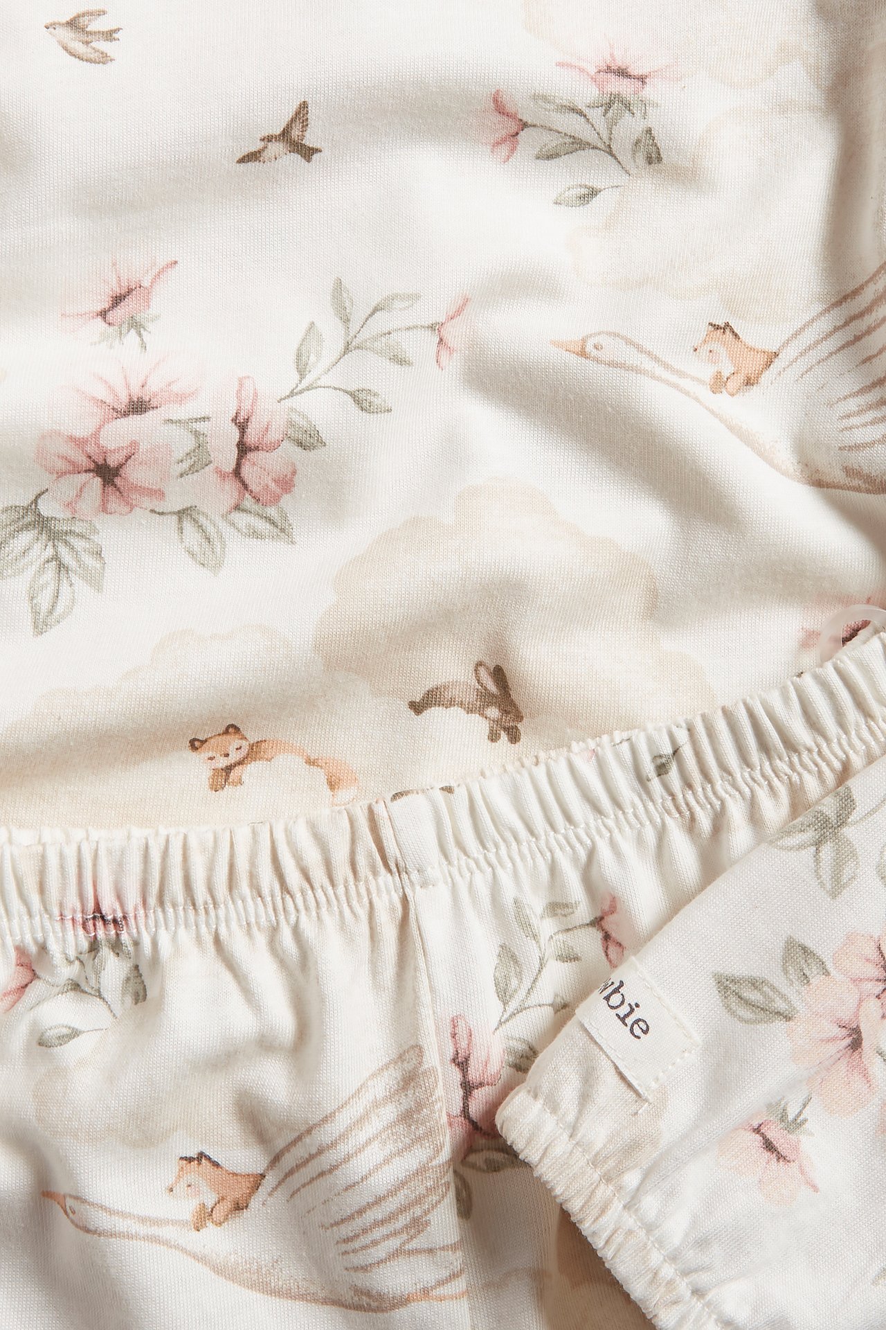 Close-up: off-white kid's cotton pyjamas, patterned with flowers, leaves, birds, bunnies, and foxes on swans.