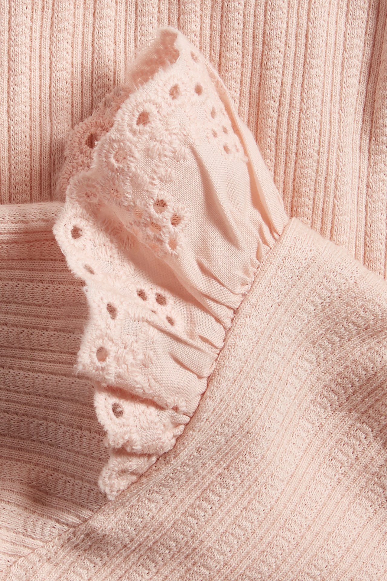 Close-up of a light pink ribbed baby bodysuit with a frill and lace detail on the shoulder.