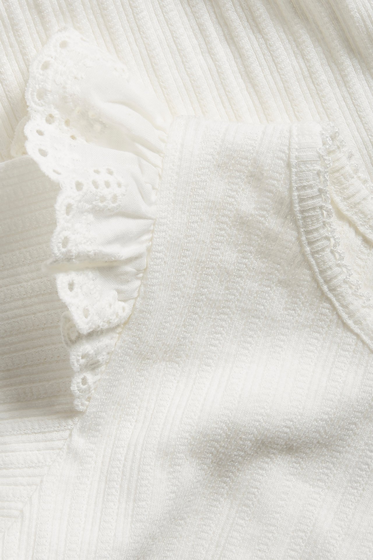 Nahaufnahme eines cremefarbenen gerippten Baby-Bodys mit Rüschen und Spitzendetail an der Schulter.
