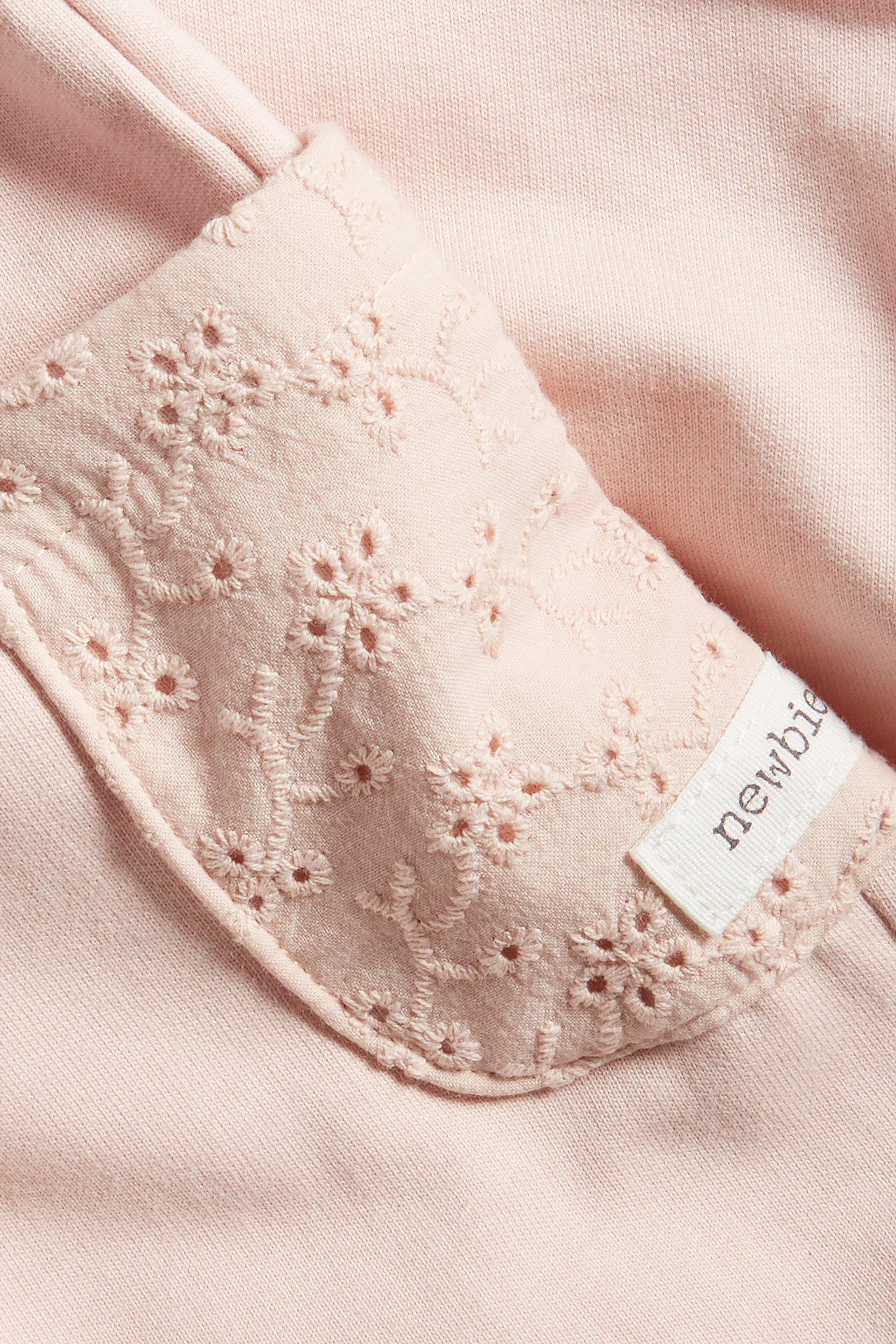 Close-up of light pink cotton jogging bottoms with a woven embroidered pocket and a small white label.