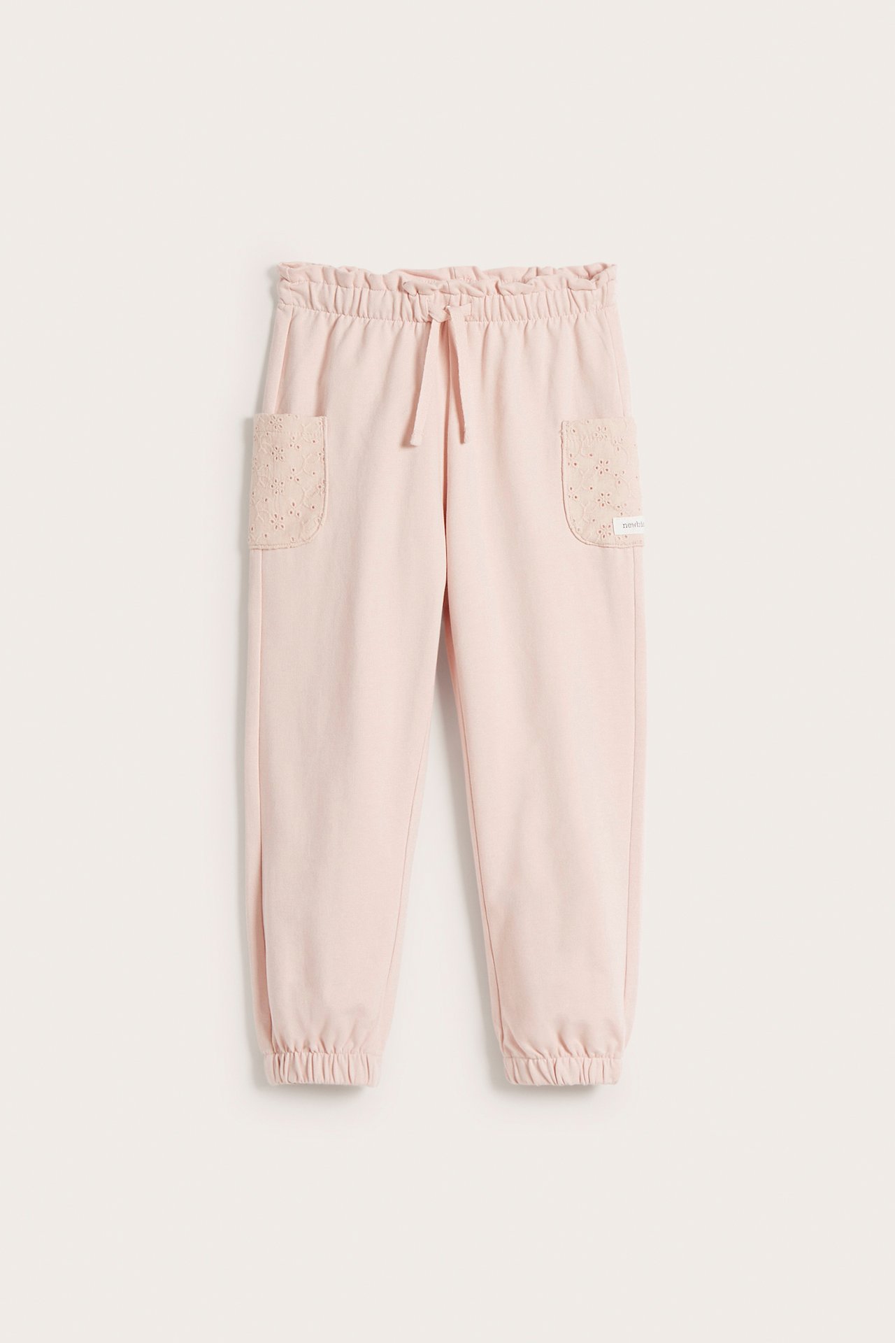 Front view of light pink cotton jogging pants for kids with elasticated drawstring waist and embroidered pockets.