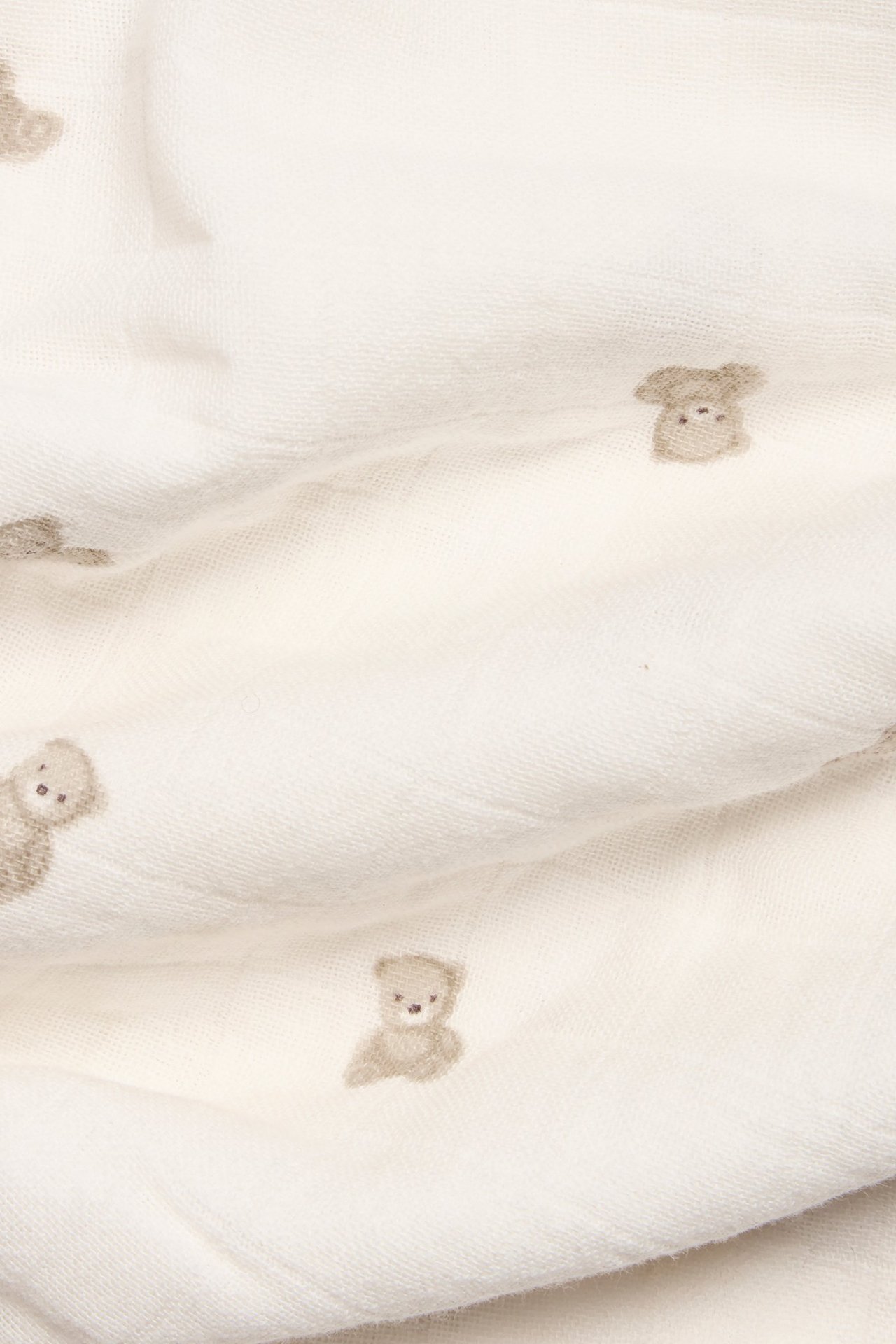 Close-up of an off-white muslin blanket with a light brown teddy bear pattern.