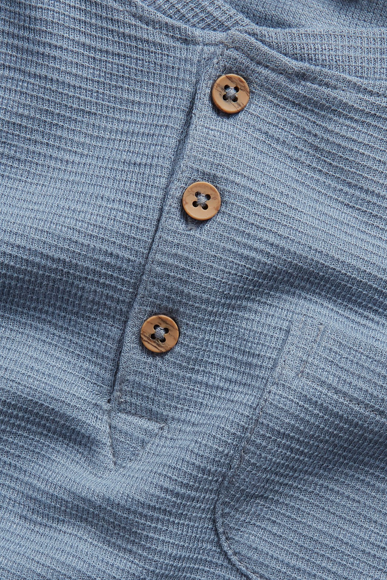 Nahaufnahme eines blauen langärmeligen Waffel-Grandad-Shirts mit drei Holzknöpfen.