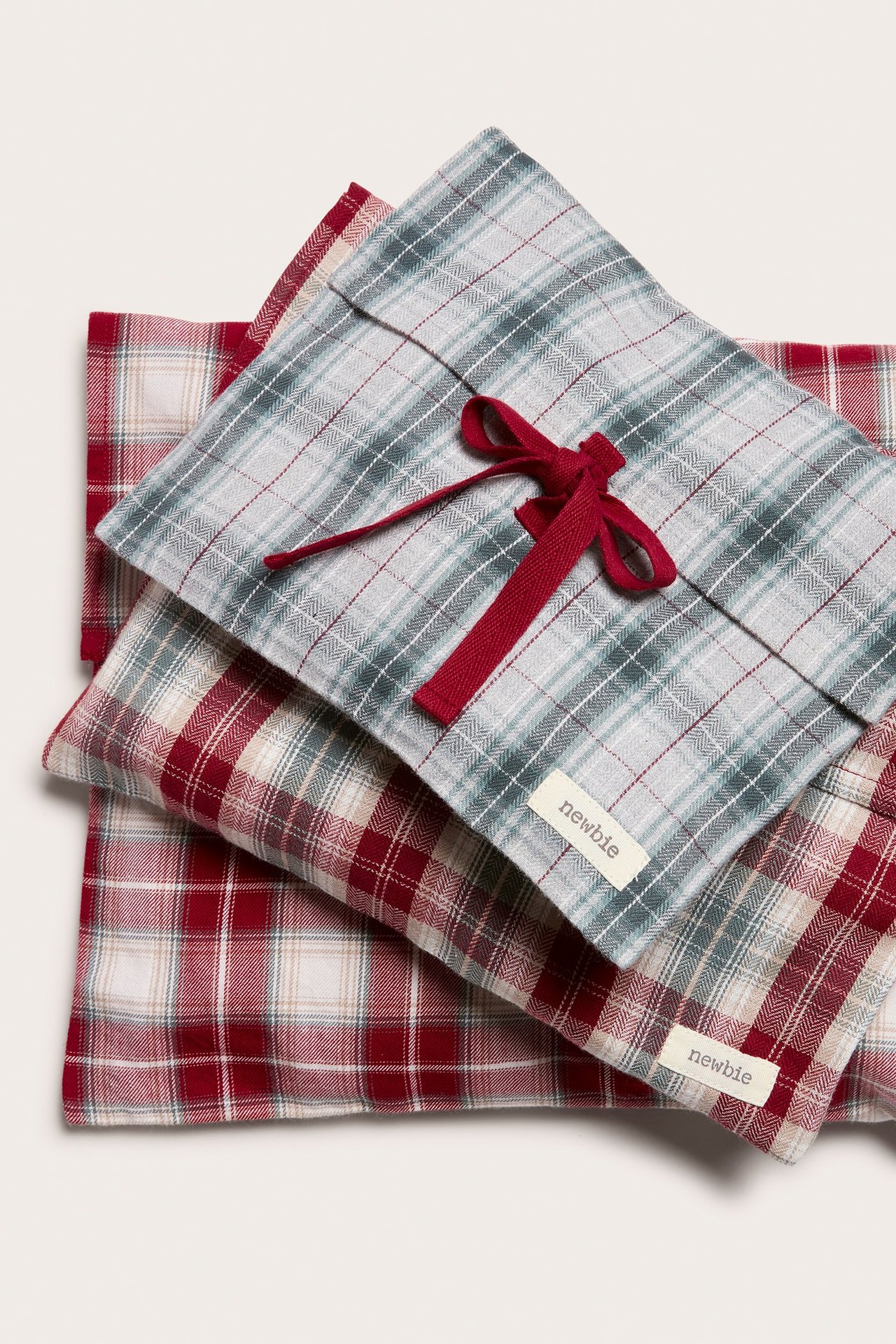 Top view of three cotton plaid gift bags. One grey-green with red ribbon, two red-beige stacked below.