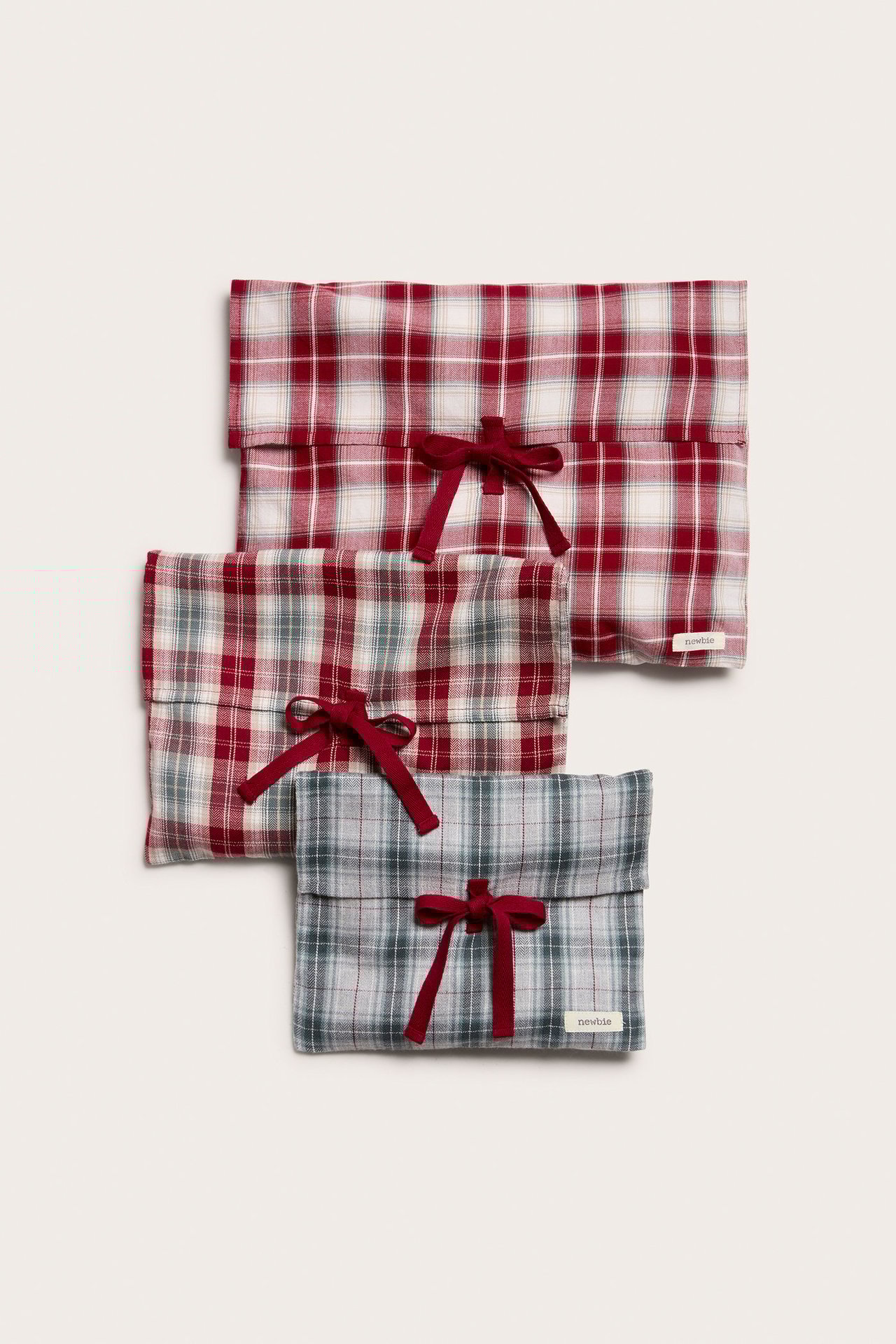 Top-down view of three plaid cotton gift bags with red ribbon ties. Patterns: red, red/grey, grey/green.