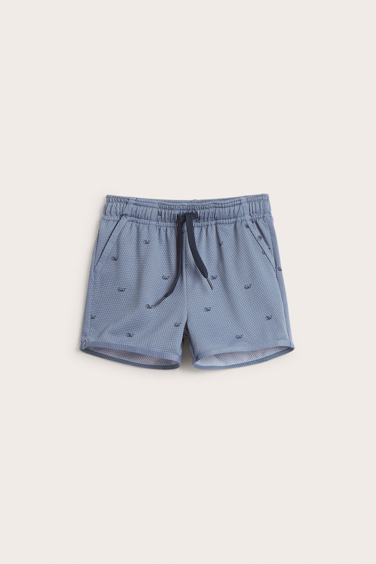 Vorderansicht blauer Kinder-Badeshorts mit strukturiertem Stoff, kleinem Fischmuster, Gummizug und dunkelblauem Kordelzug.