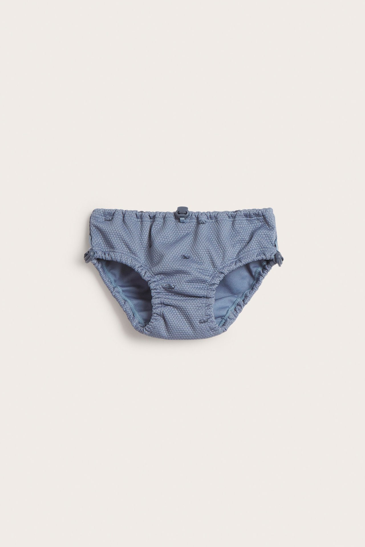 Front view of blue baby swim briefs with a subtle fish pattern, elasticated waist, and adjustable stoppers.