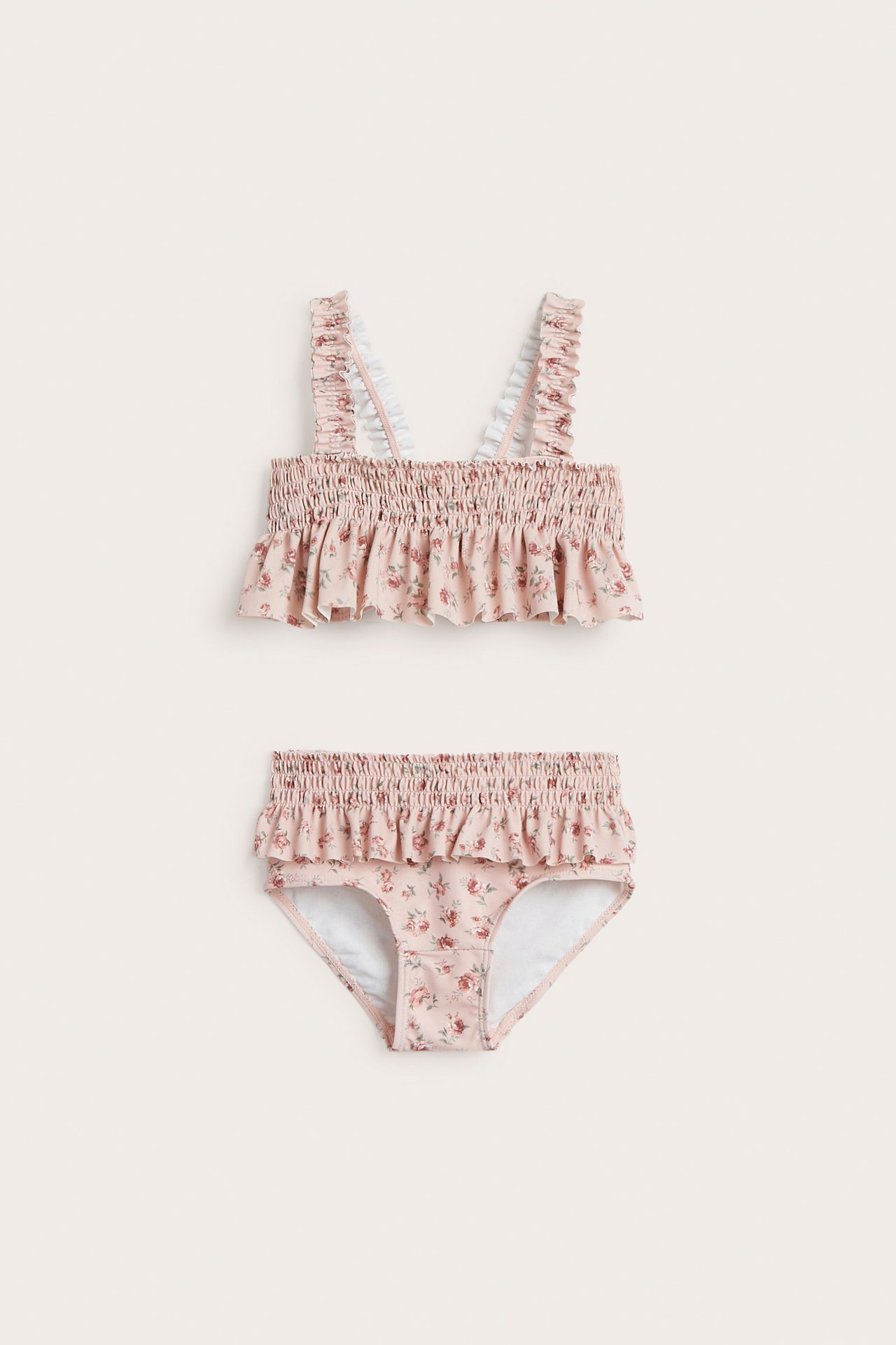Front view of a kid's pink floral bikini with smocked details and ruffles on top and bottom.