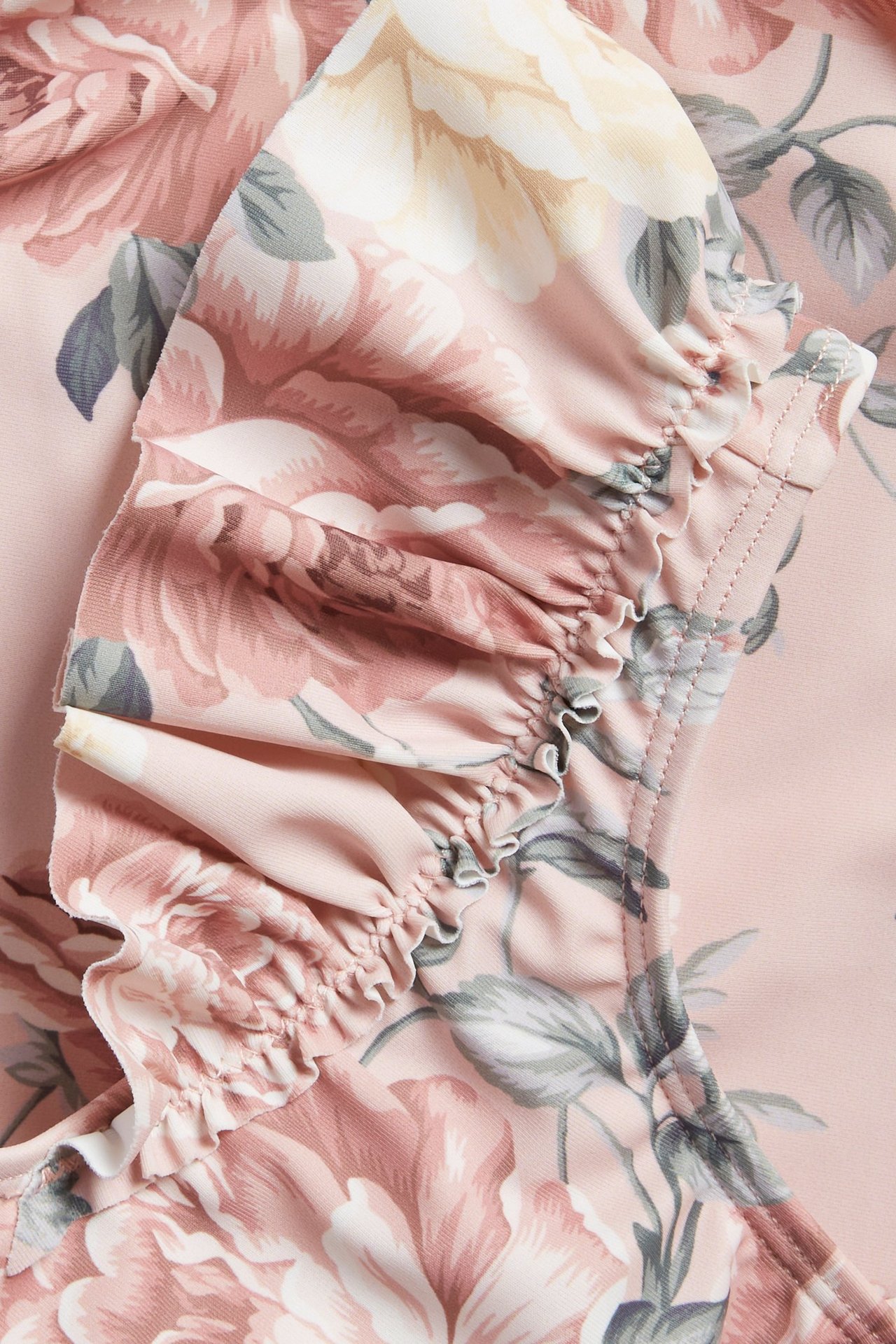 Nahaufnahme eines pinkfarbenen geblümten Kinderbadeanzugs mit Rüschen am Schulterträger.