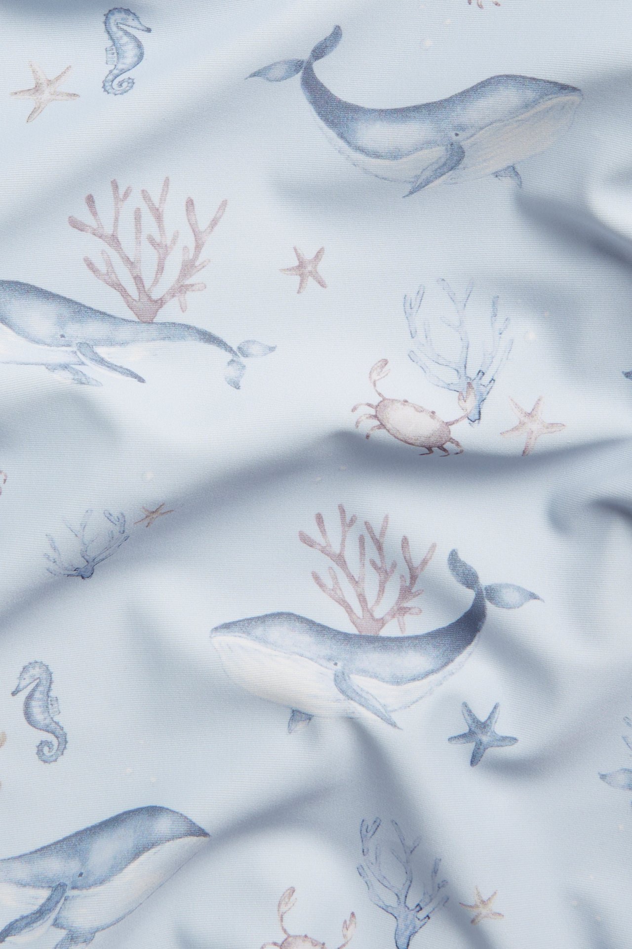 Close-up of a light blue patterned UV top fabric with whales, seahorses, crabs, starfish, and coral.
