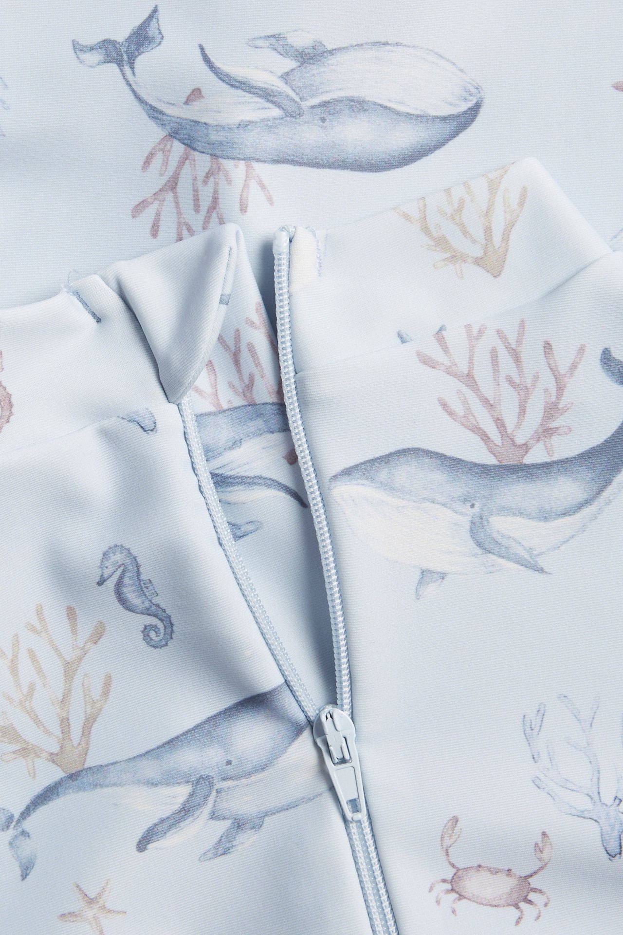 Close-up of a light blue patterned UV suit with whales and coral, featuring a zipper.