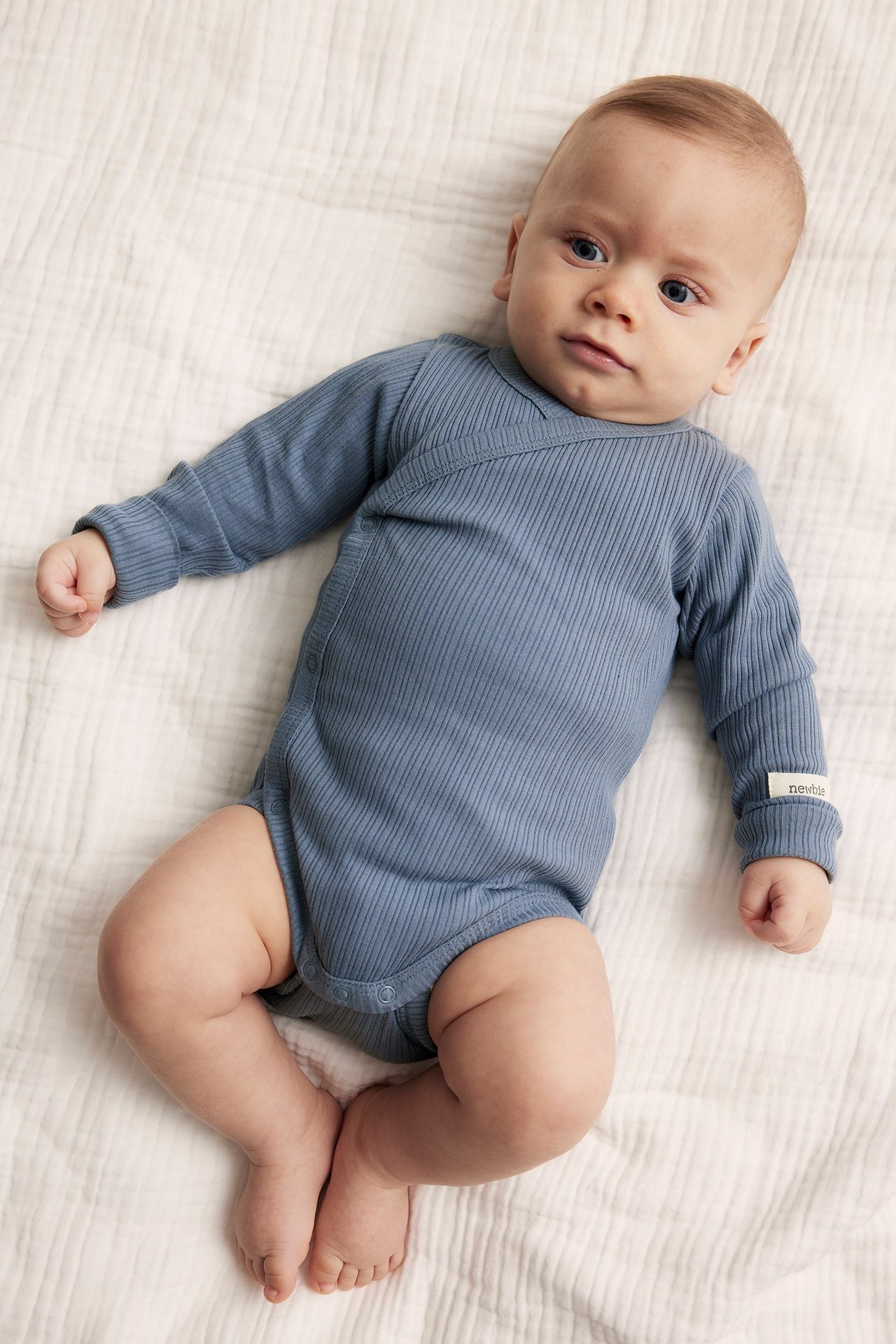Top view of a baby wearing a blue ribbed cotton wrap-around bodysuit with snap buttons.