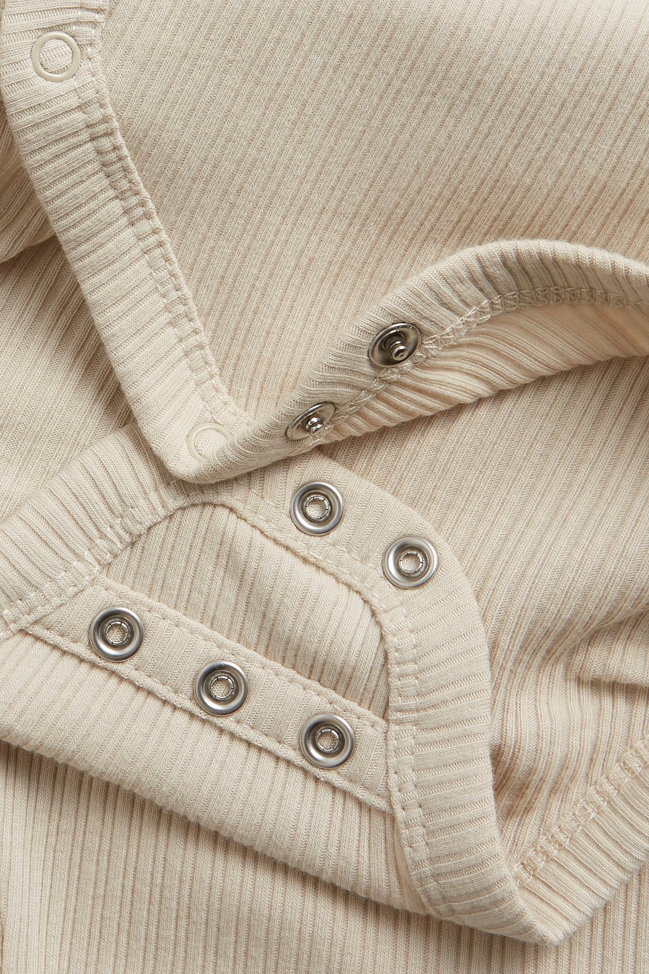 Close-up of a beige ribbed wrap-around baby bodysuit with silver snap buttons.