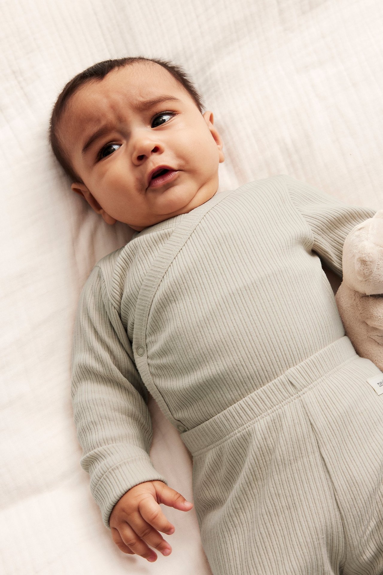 Nahaufnahme eines Babys in einem beigen gerippten Wickelbody mit Druckknöpfen und passender Hose.