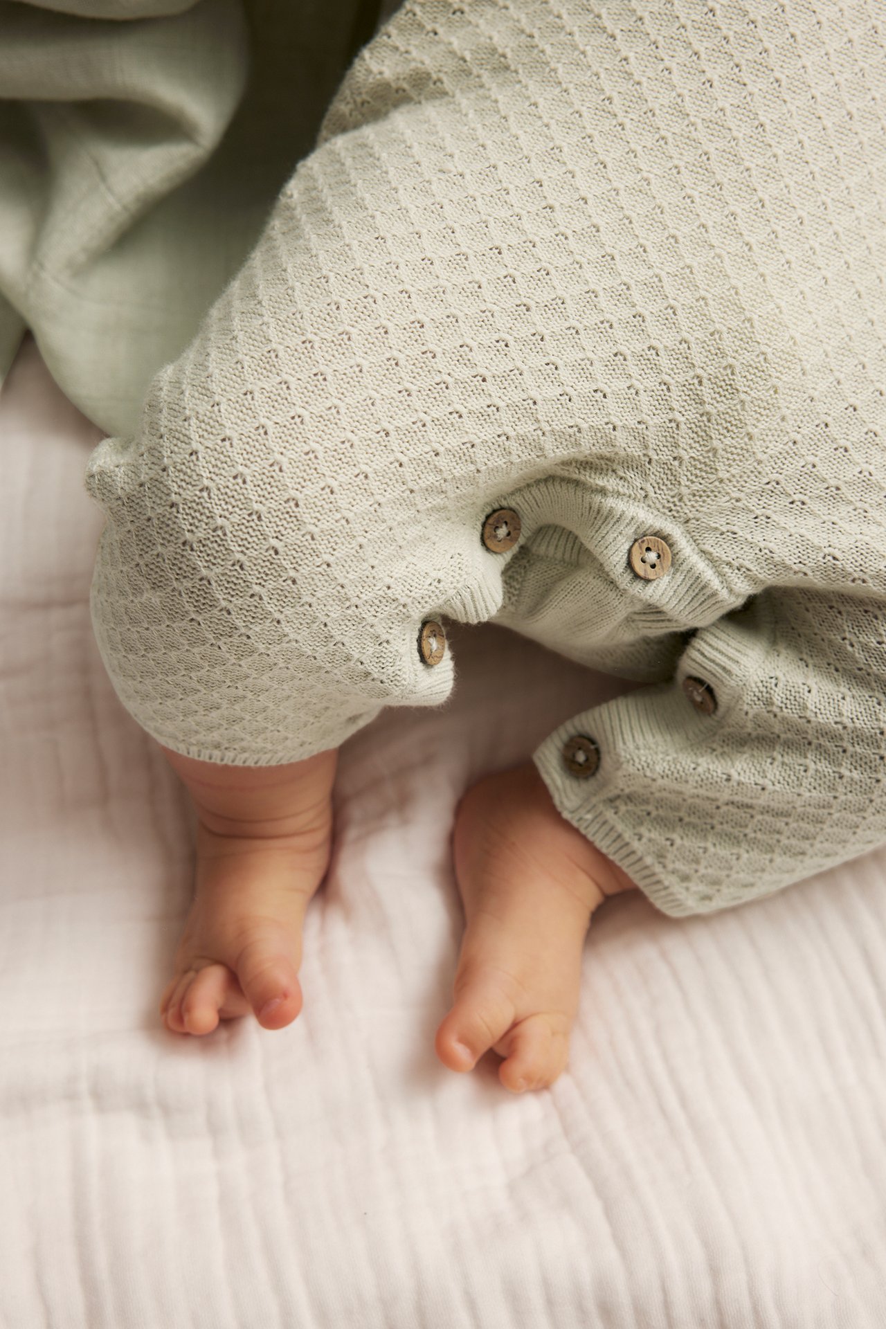 Close-up of a baby wearing a light green knitted cotton jumpsuit with wooden buttons.