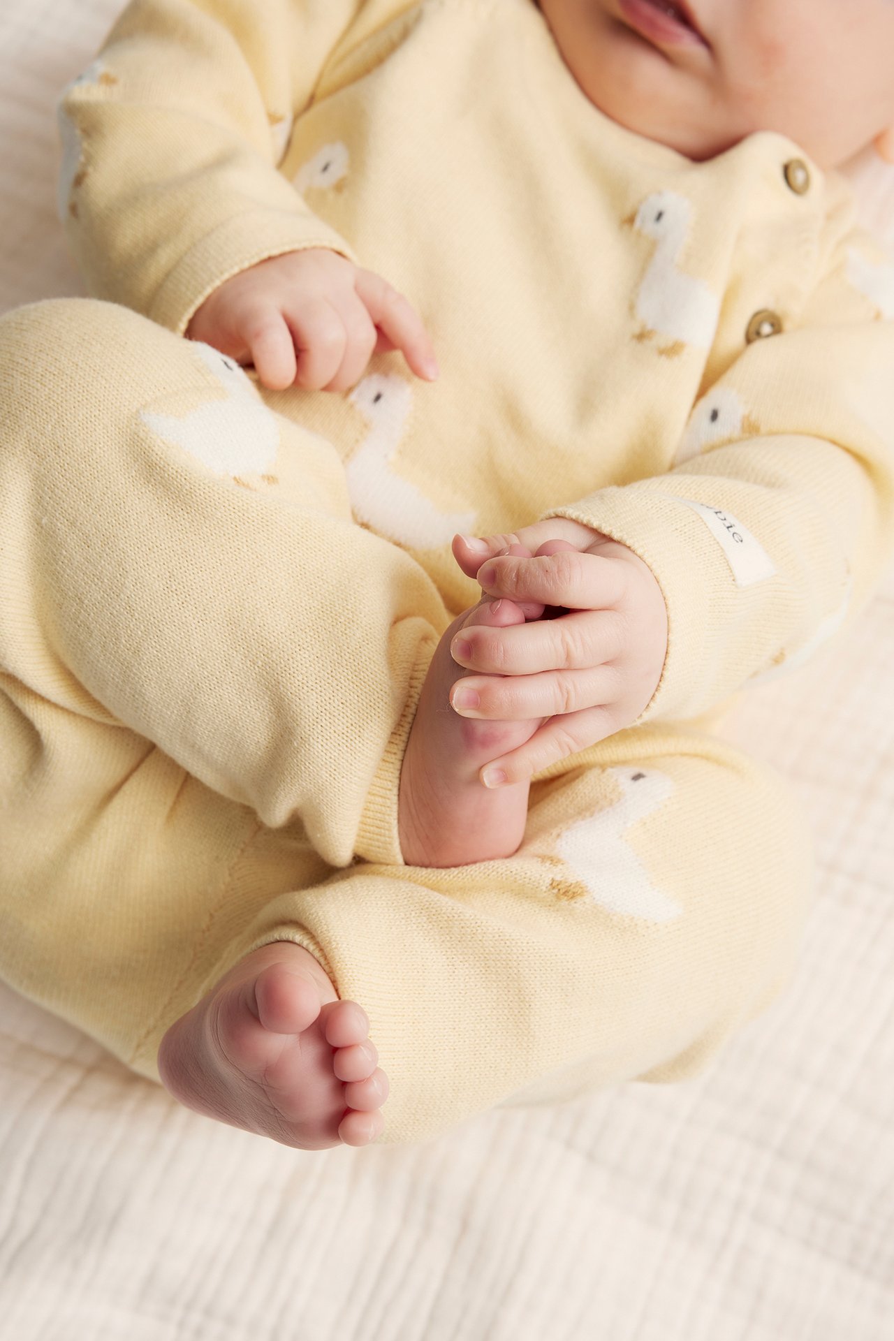 Nahaufnahme von Baby in gelben gestrickten Enten-Leggings und passendem Oberteil mit Zierknöpfen.