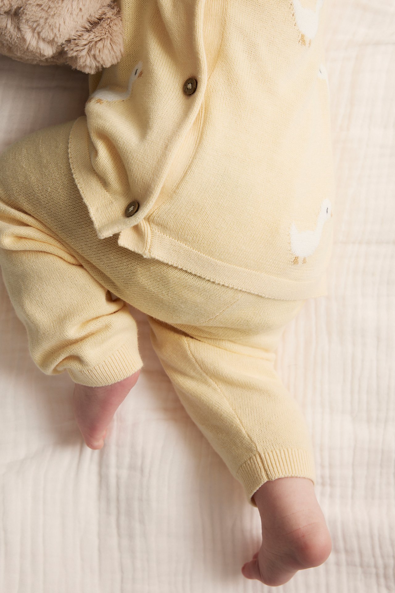 Draufsicht auf ein Baby in gelben gestrickten Enten-Leggings und passender Strickjacke mit Knöpfen.