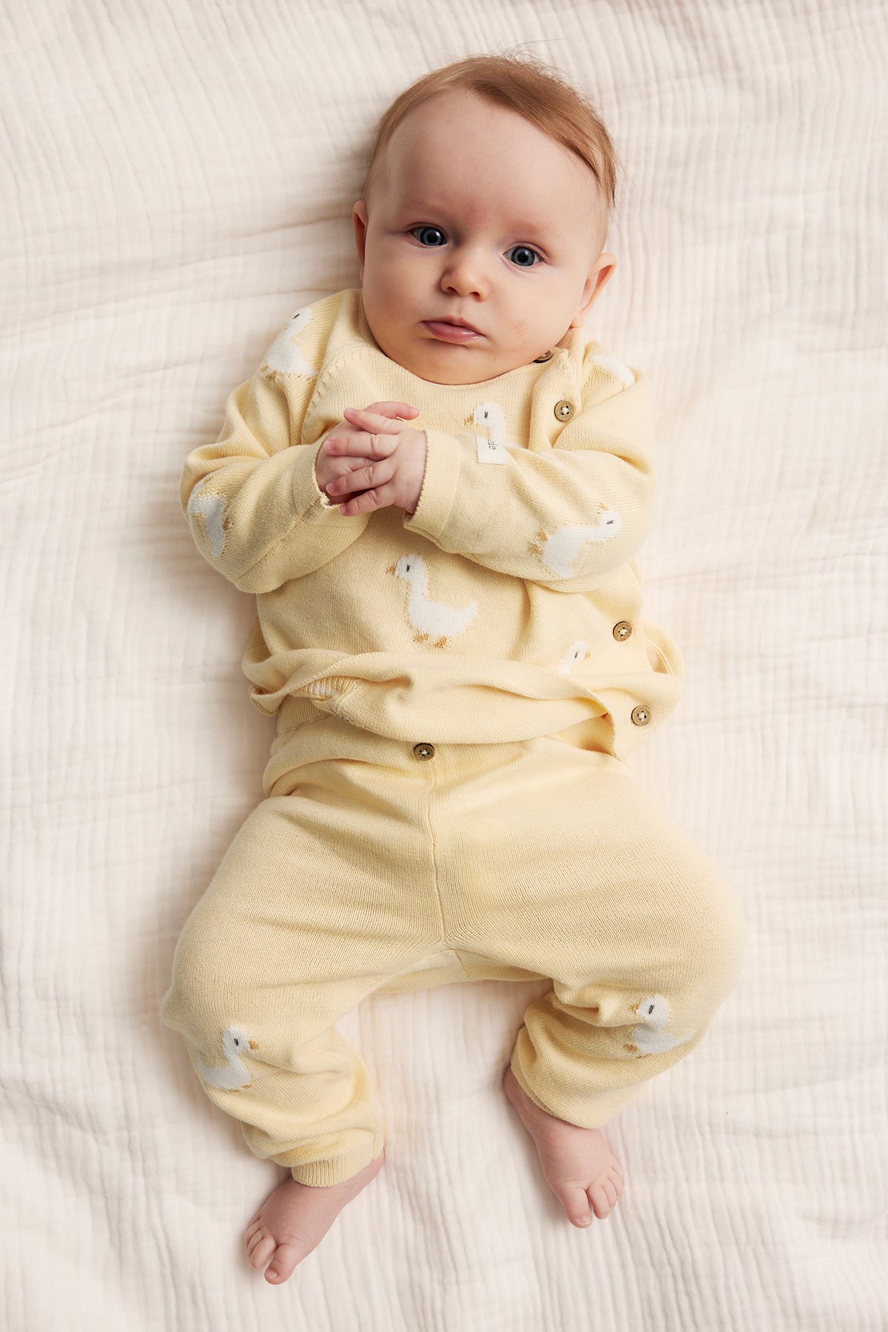 Vorderansicht eines Babys in gelben gestrickten Baumwoll-Leggings mit Entenstickerei und passendem Oberteil.