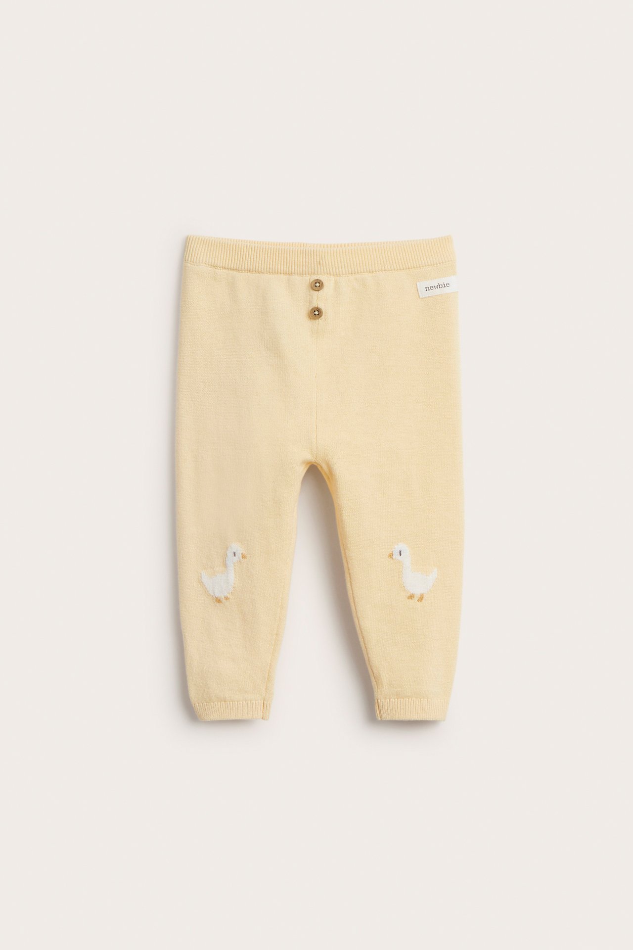 Vorderansicht von babygelben gestrickten Baumwoll-Leggings mit zwei Zierknöpfen und Entenstickerei an den Knien.