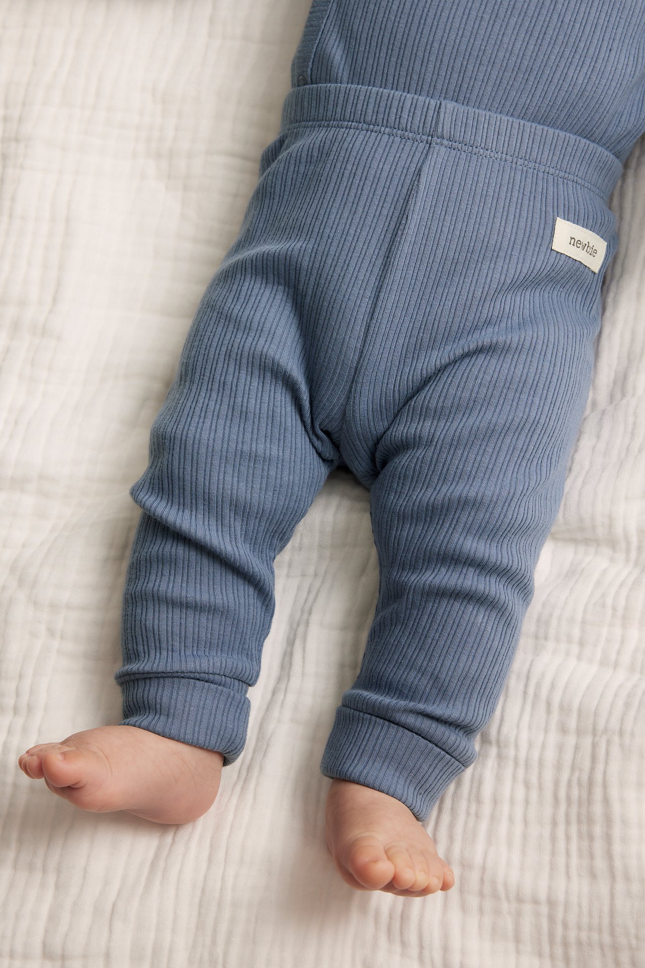 Close-up of baby wearing blue ribbed leggings with elastic waist and folded cuffs, and a matching top.