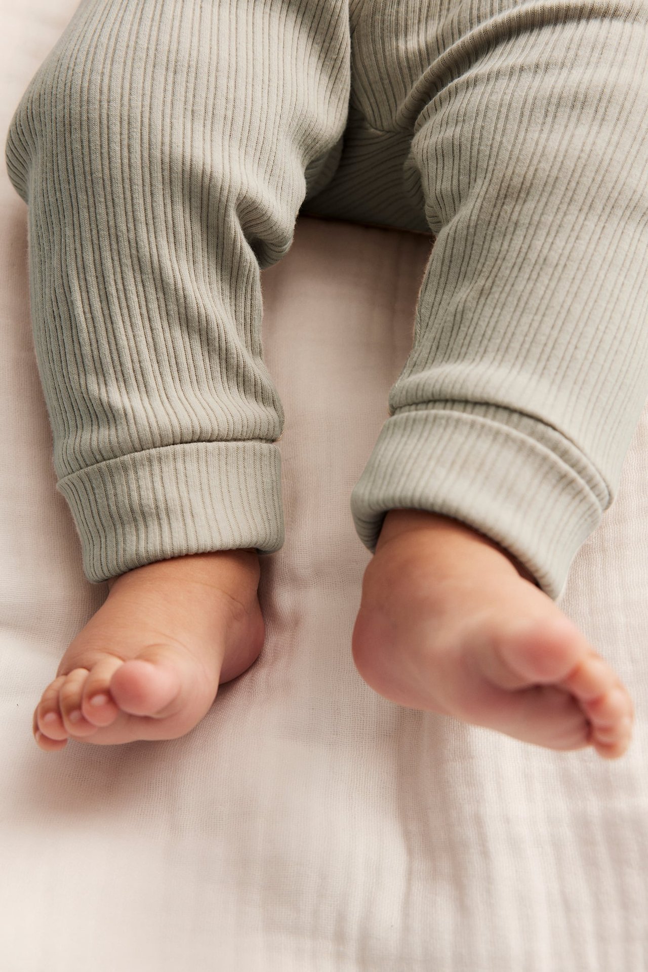 Nahaufnahme von Babybeinen in hellbeigen gerippten Leggings mit umgeschlagenen Bündchen.