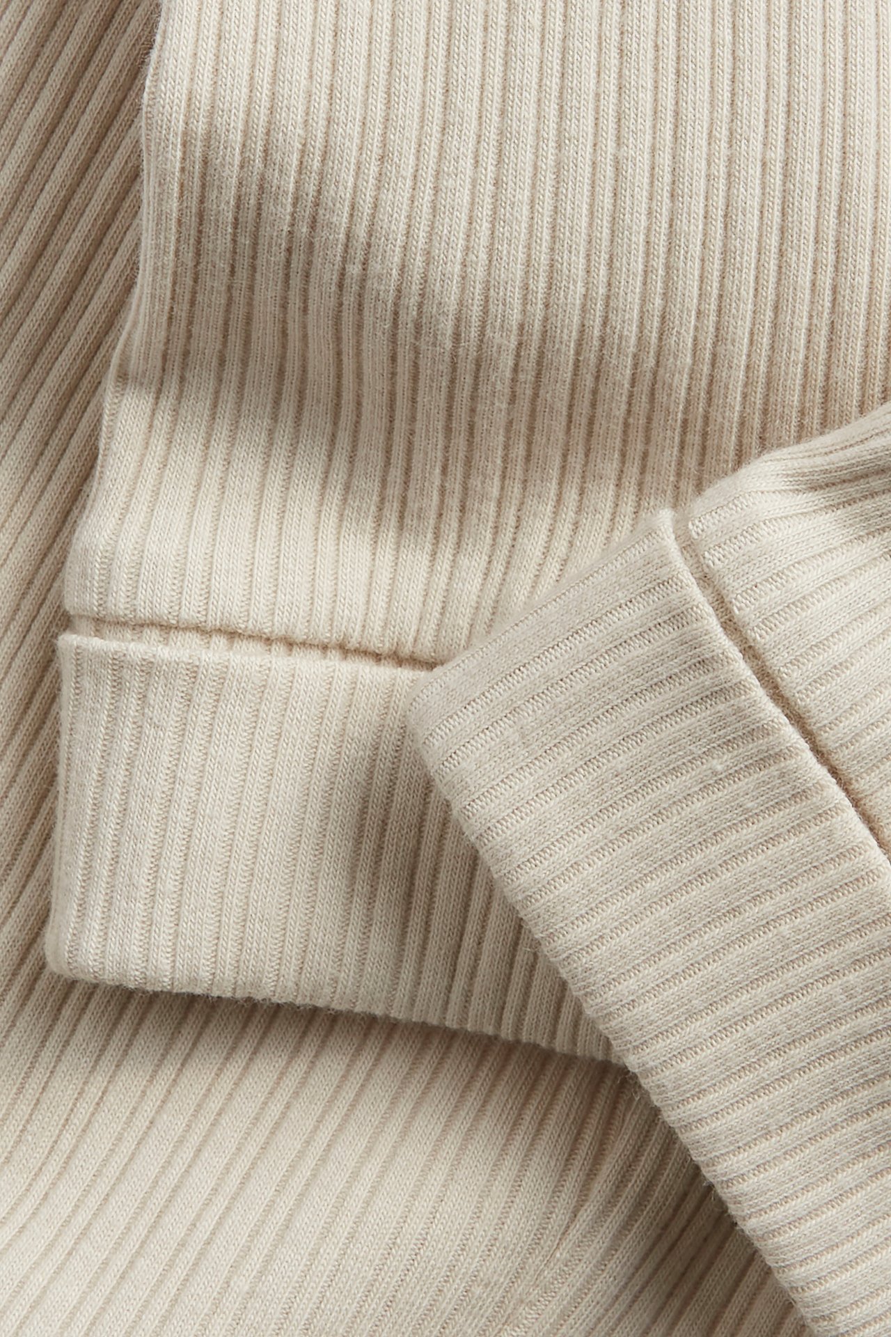 Close-up of beige ribbed baby leggings with folded cuffs.