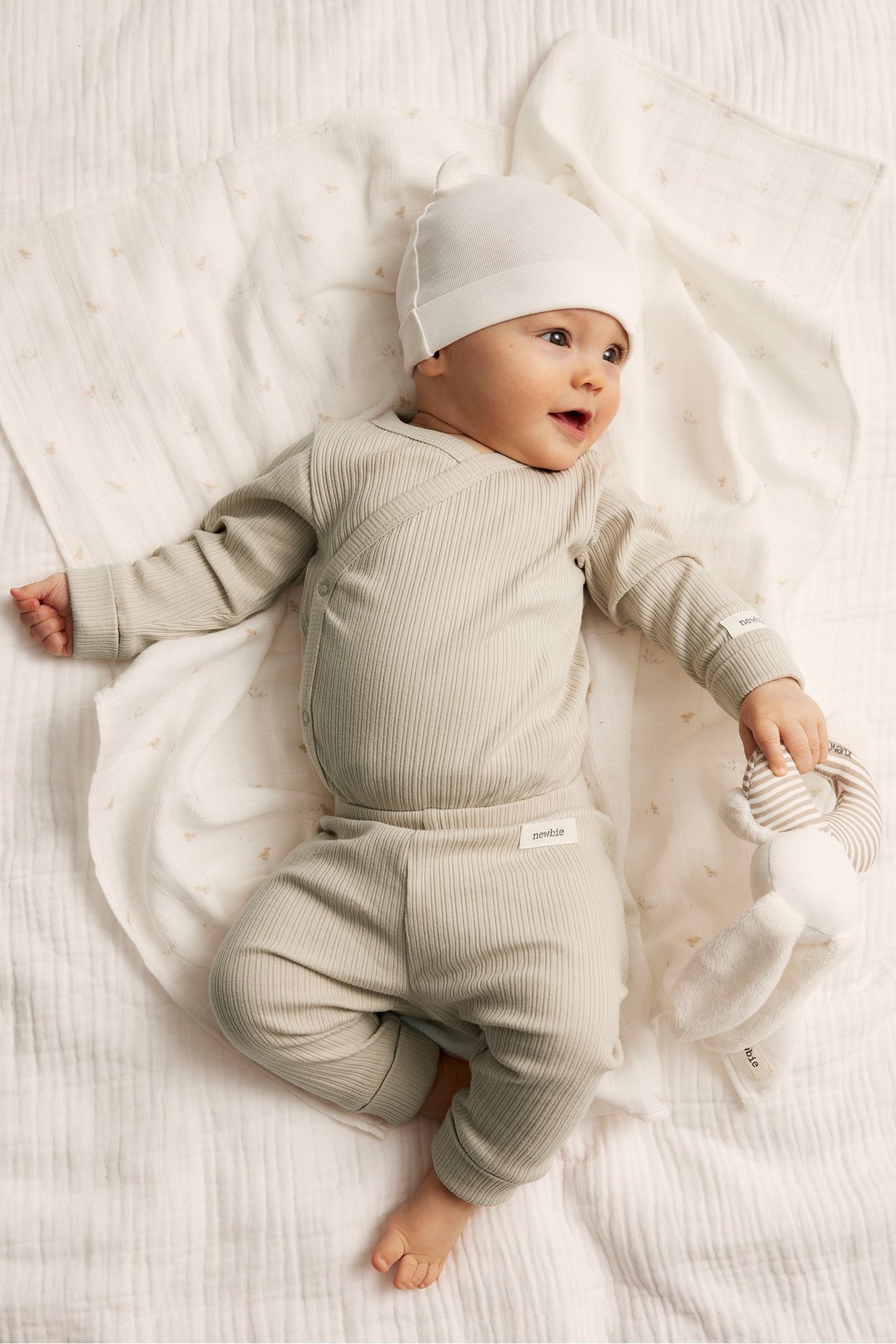 Front view of a baby wearing beige ribbed leggings, a matching ribbed bodysuit, and a white beanie.