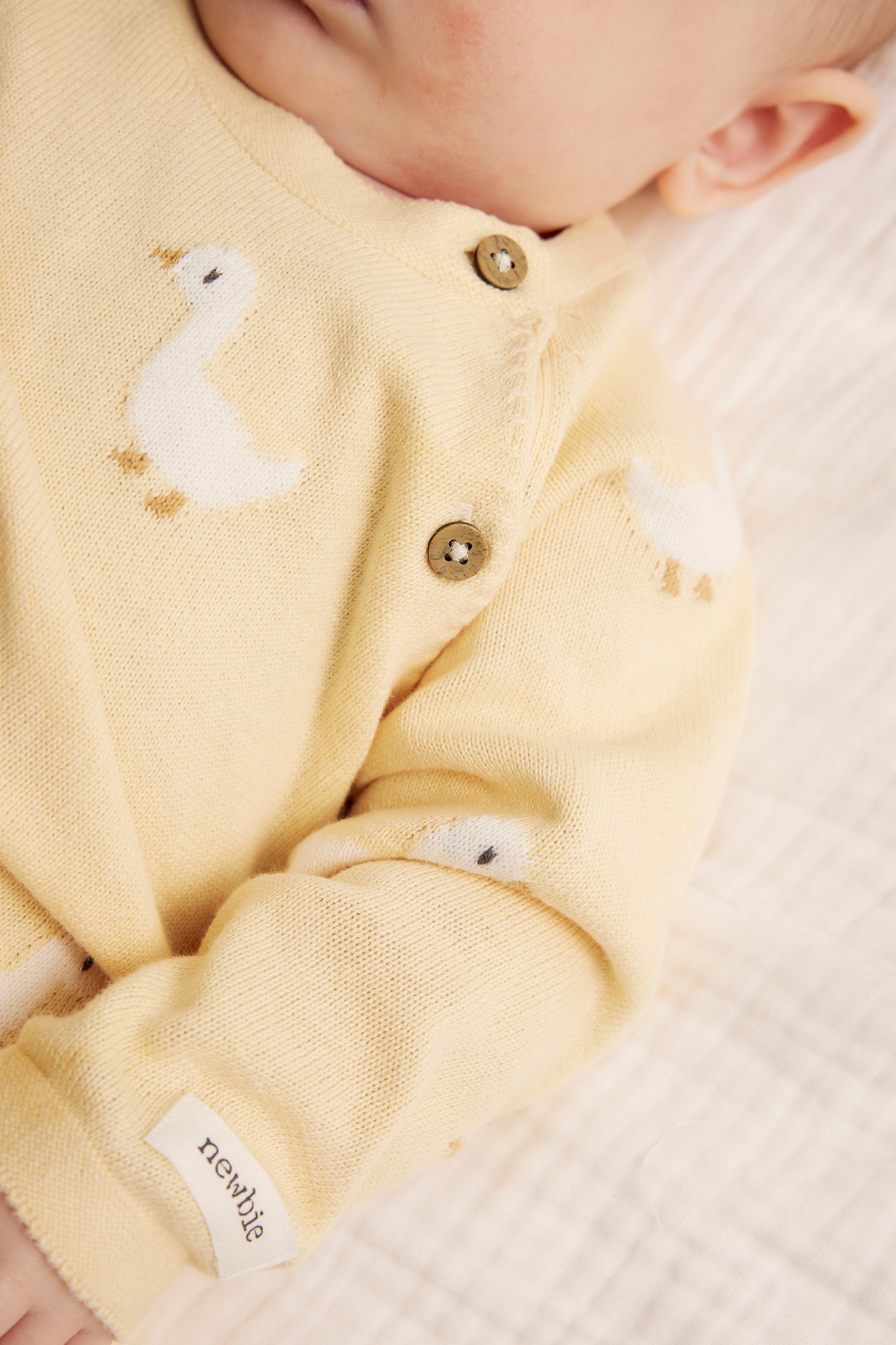 Close-up of a baby in a yellow knitted cotton cardigan with white duck patterns and wooden side buttons.
