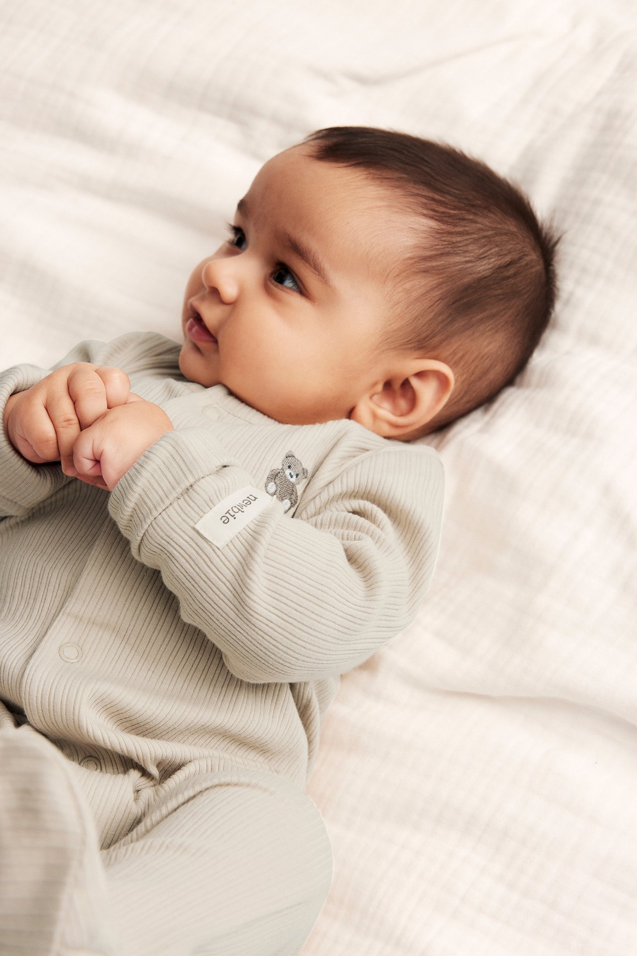 Close-up of a baby wearing a beige ribbed pyjamas with snap buttons and a teddy bear embroidery.