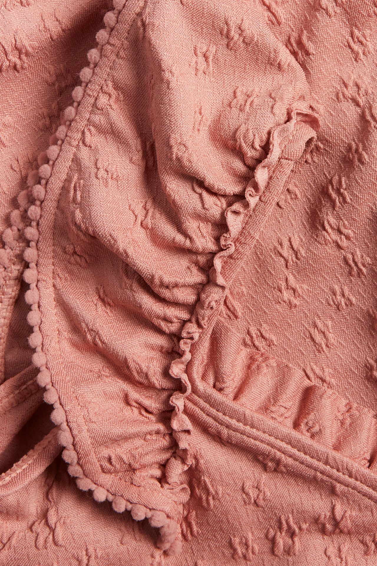 Close-up of a pink swimsuit with floral textured fabric, large ruffles, and a pom-pom trim.