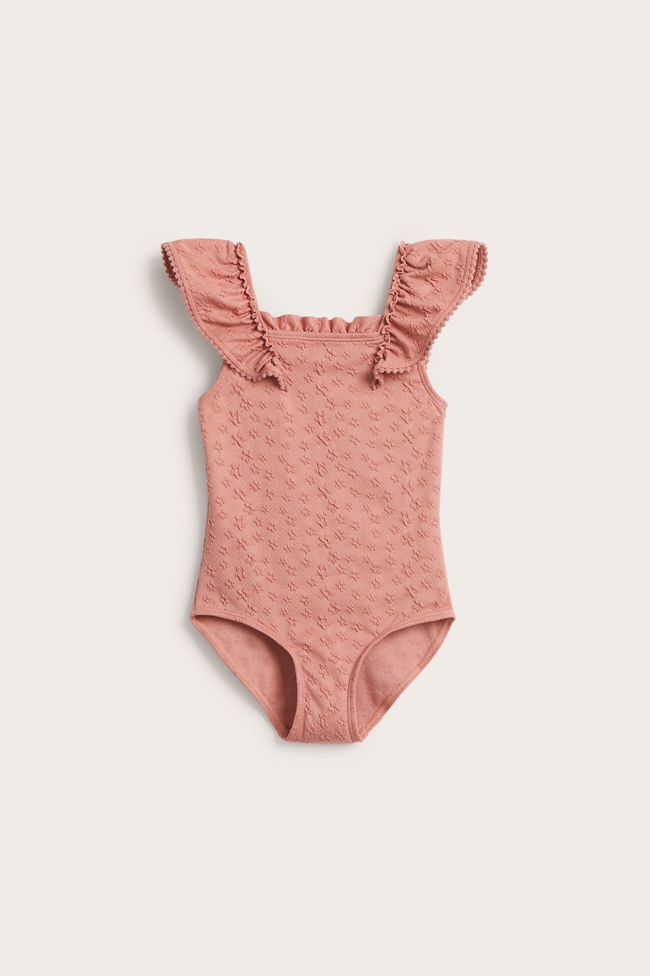 Front view of a kid's pink swimsuit with a floral texture and large ruffled shoulders with scalloped edges.