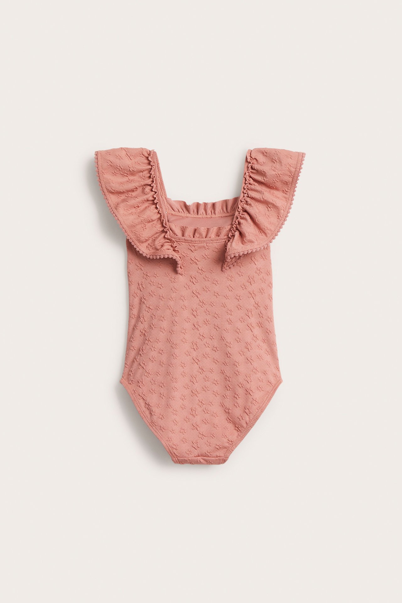 Front view of a kid's pink swimsuit with large ruffled shoulders and a subtle floral texture.