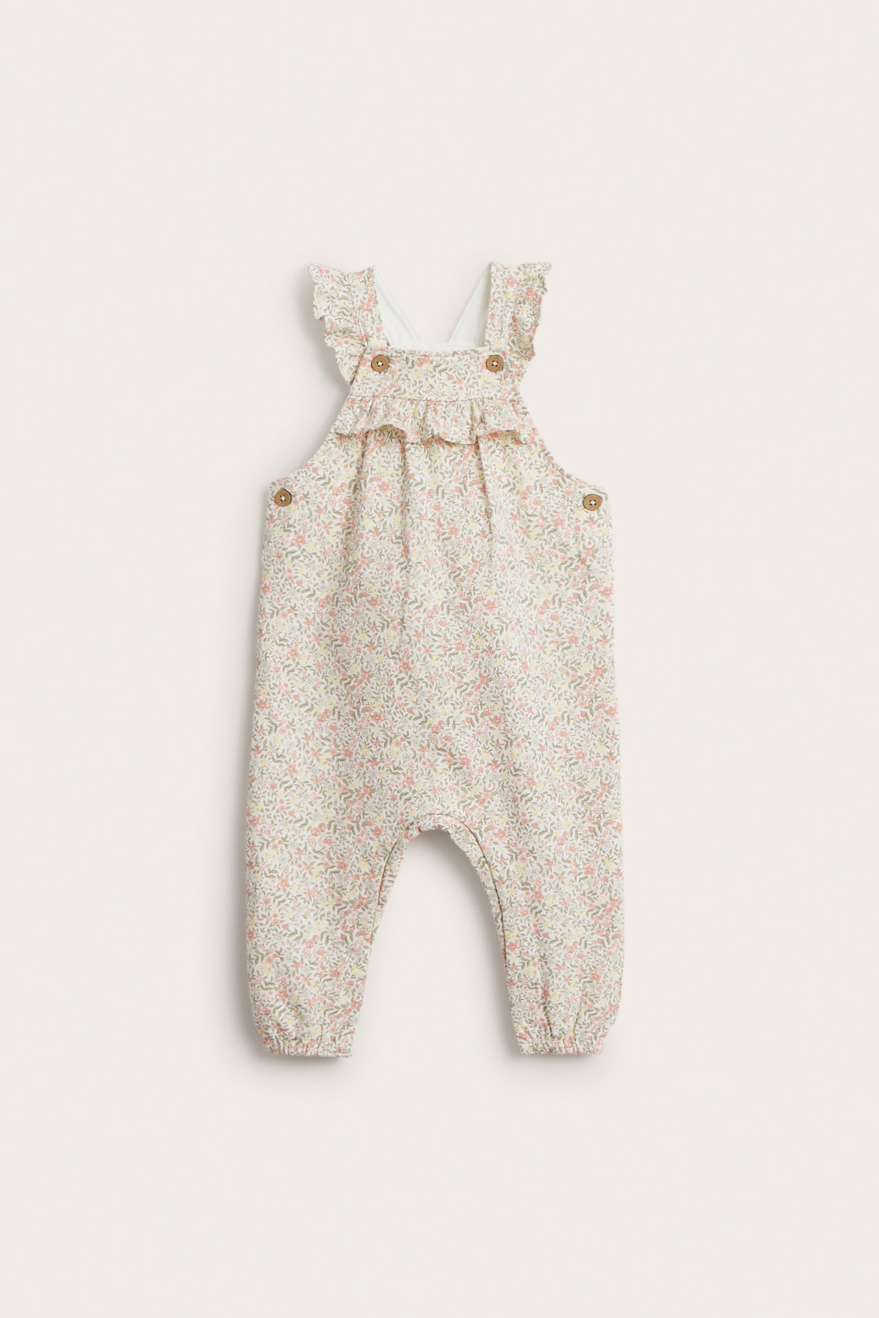 Vorderansicht von baby off-white geblümten Jersey-Latzhosen mit Rüschen, verstellbaren Trägern und Seitenknöpfen.