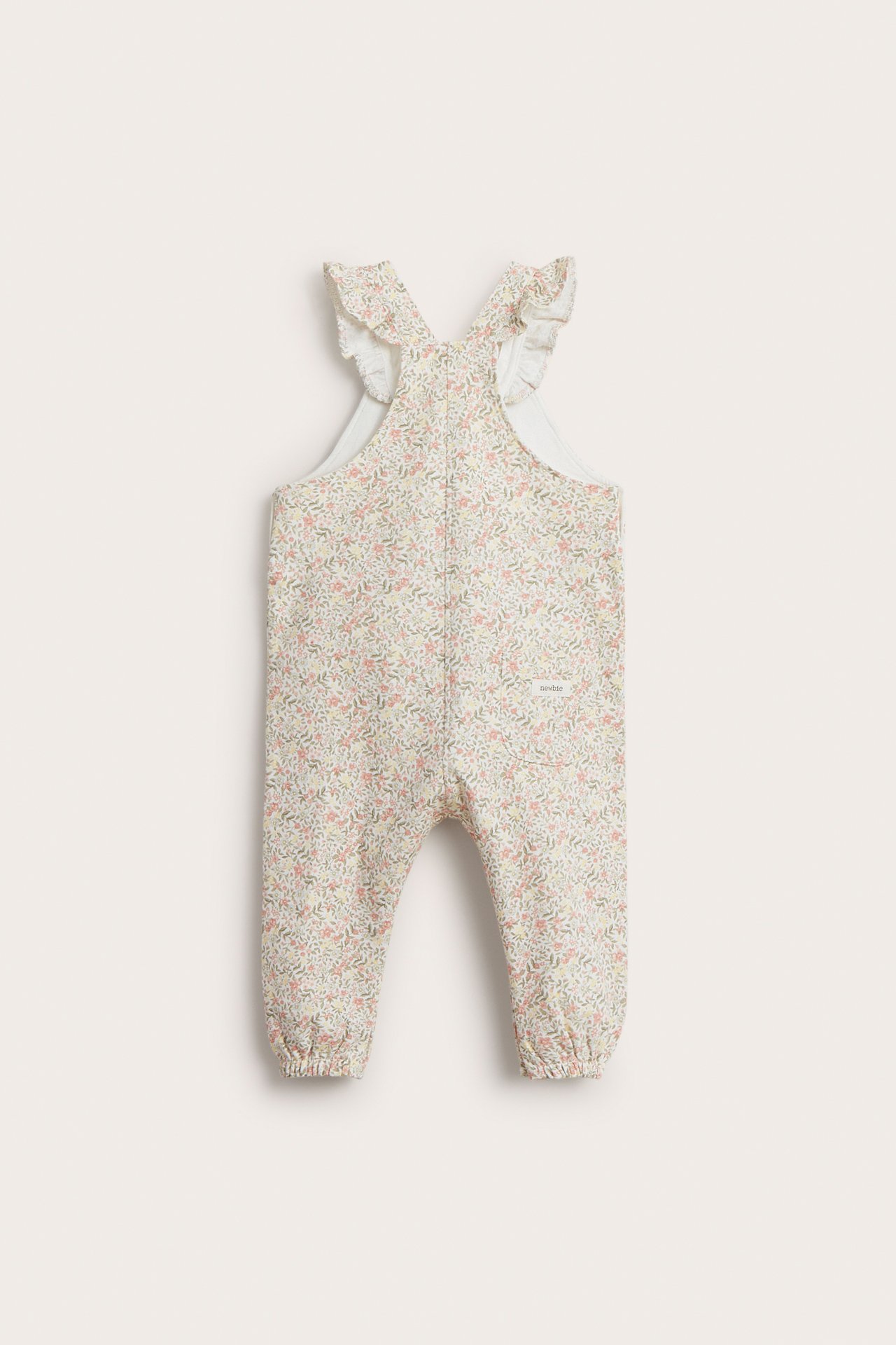Rückenansicht: Baby-Overall aus cremeweißer Baumwolle mit Blumenmuster, Rüschenträgern und Gummizug.