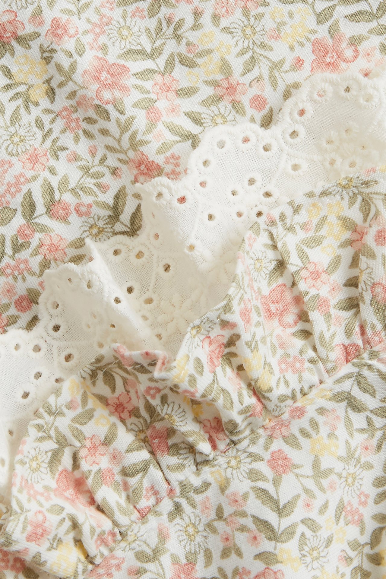 Nahaufnahme eines cremefarbenen Baumwollkleides mit Blumenmuster, Rüsche und weißer Lochstickerei-Spitzenborte.