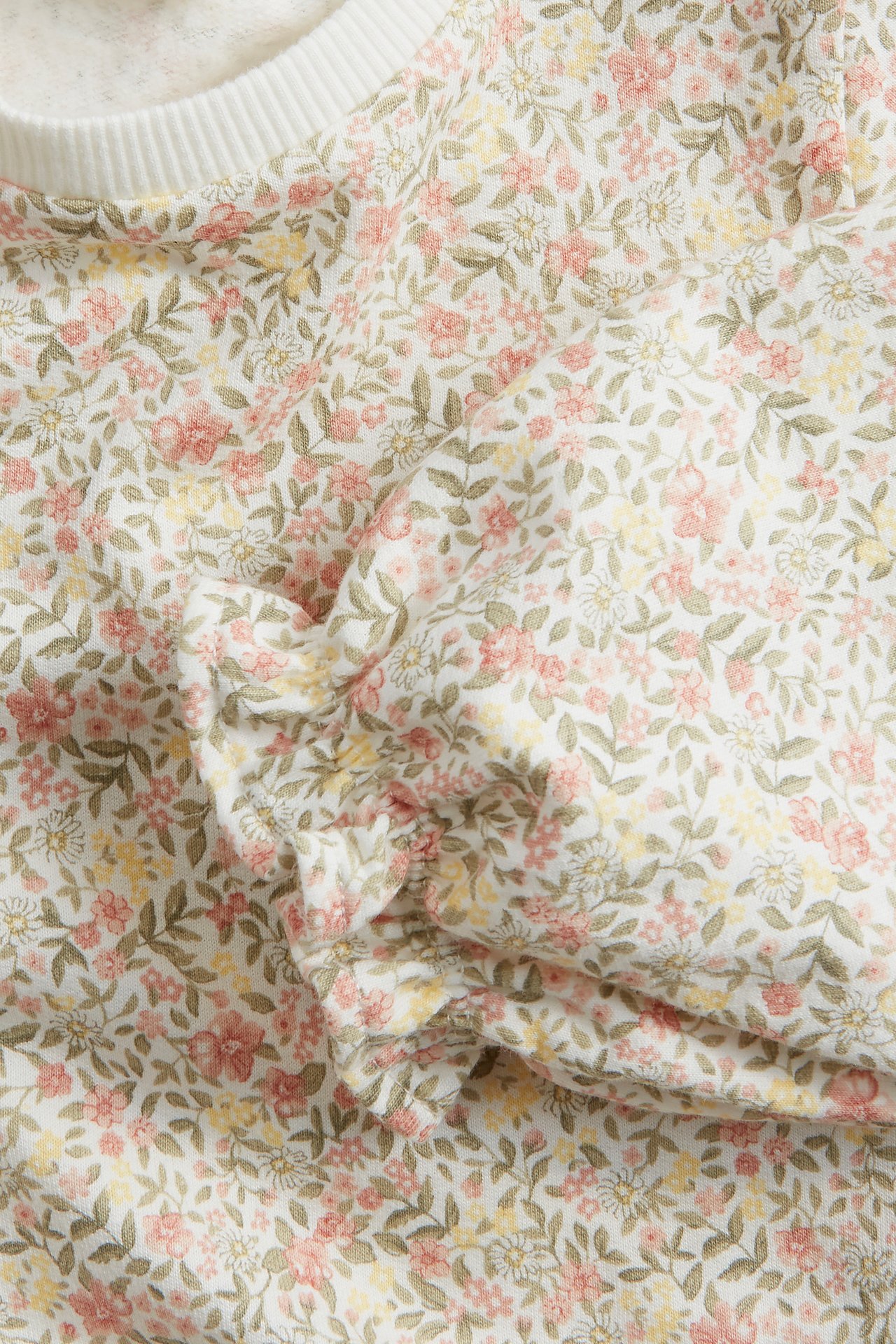 Close-up of an off-white cotton sweatshirt with a floral print, ribbed neck, and frilled puff sleeve.