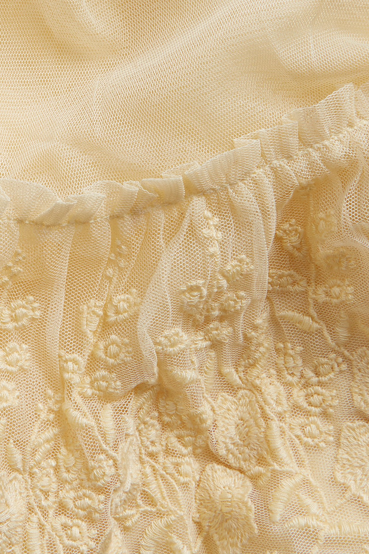 Nahaufnahme eines gelben Mesh-Rocks mit gestickten Blumenmustern und Rüschenkante.