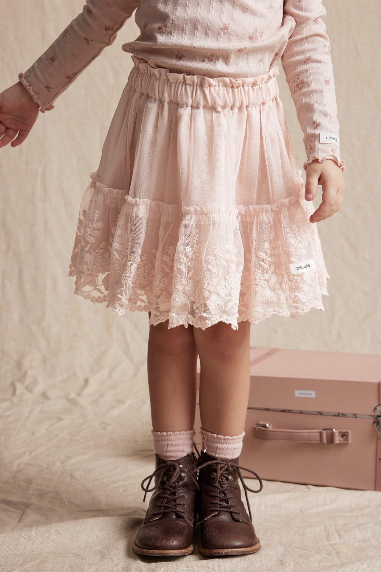 Kind in hellrosa Mesh-Rock mit Stickrüschen, Blumentop, rosa Socken, braunen Stiefeln.