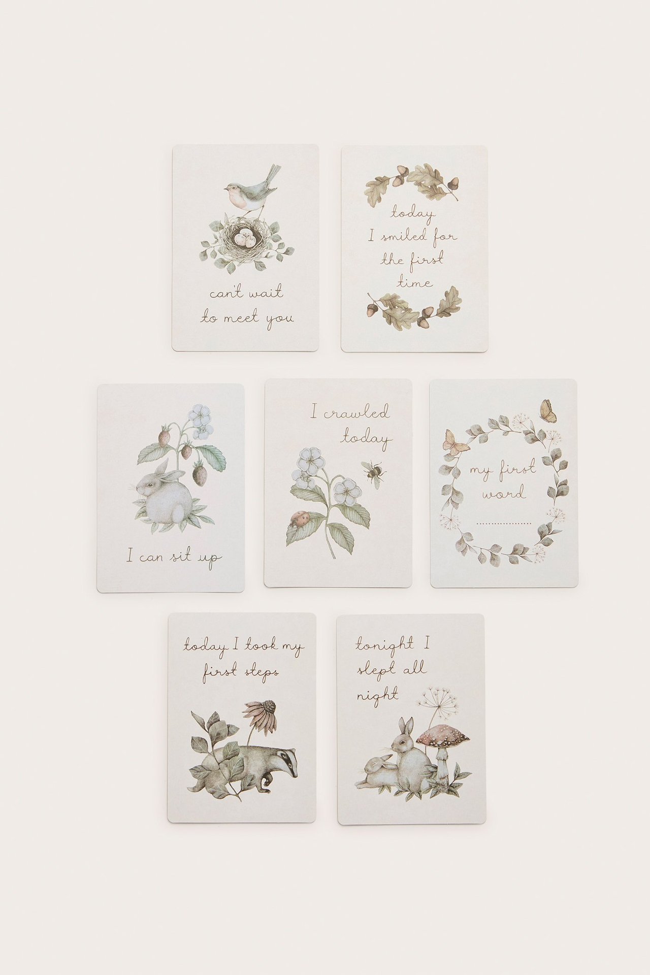 Draufsicht auf sieben cremefarbene Baby-Meilensteinkarten aus Papier mit Tier- und Naturmotiven.