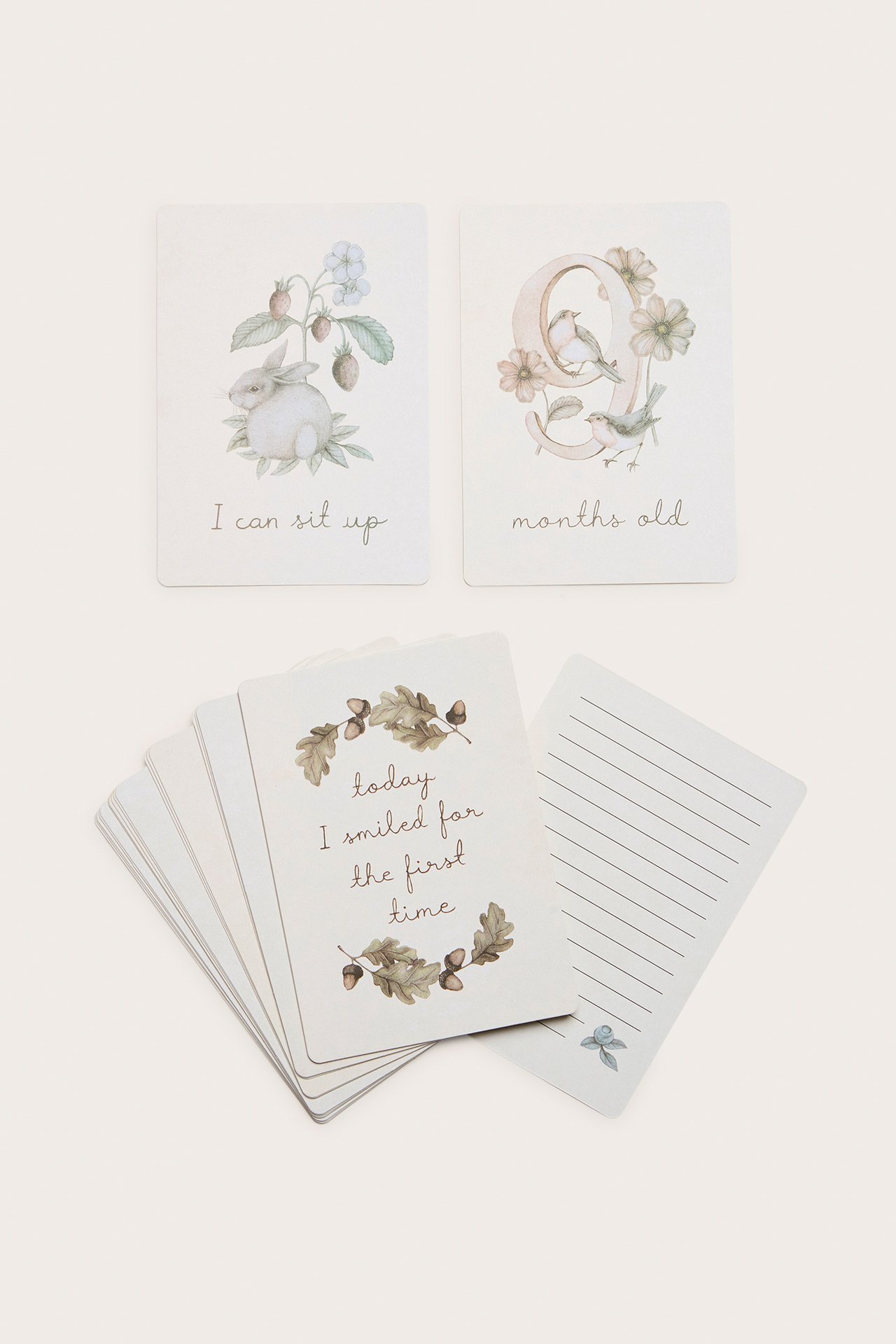 Draufsicht auf cremeweiße Baby-Meilensteinkarten aus Papier mit Tier- und Naturmustern, einige mit Text.