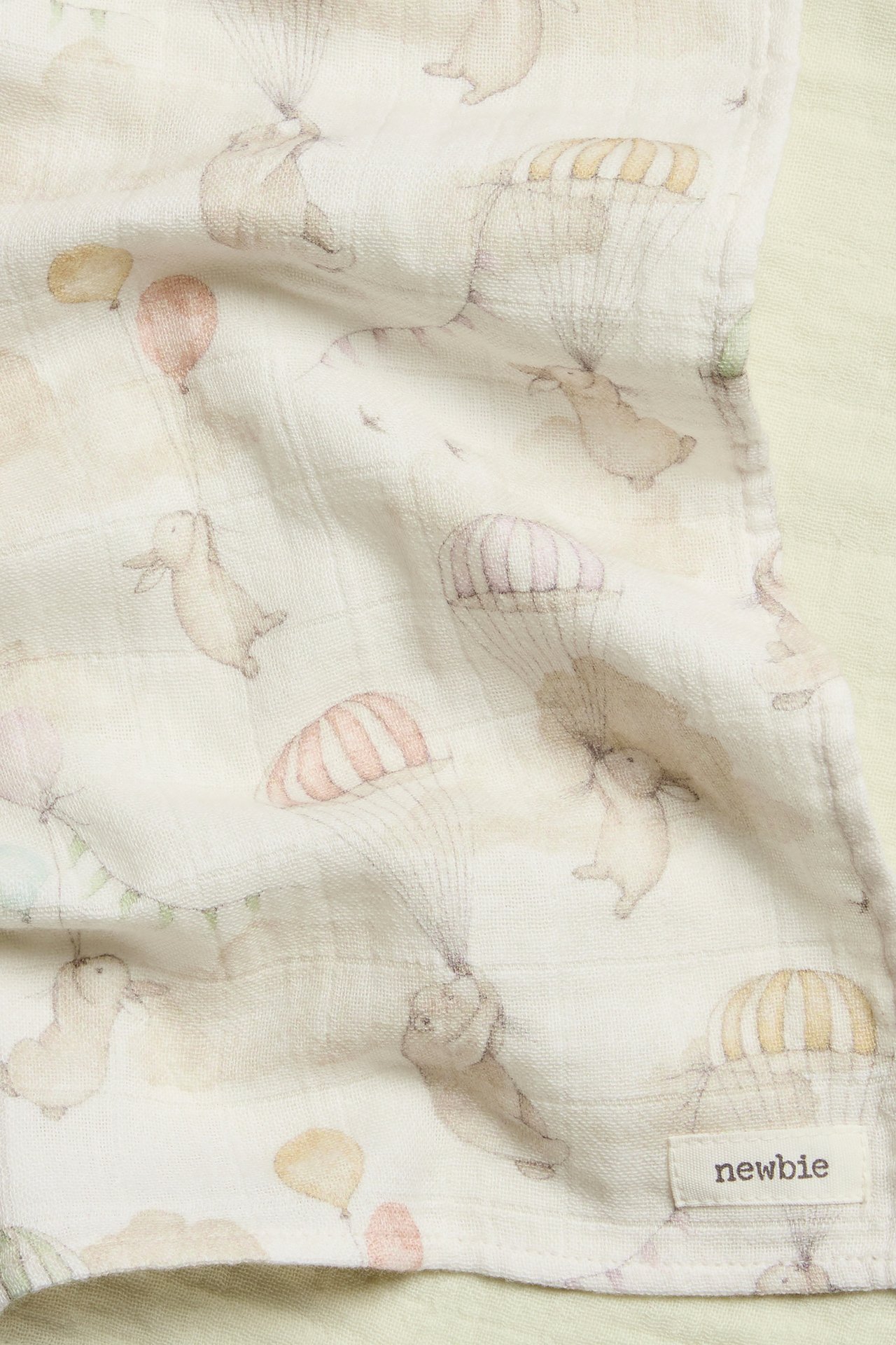 Close-up view of an off-white muslin blanket with a pattern of bunnies, parachutes, and balloons.