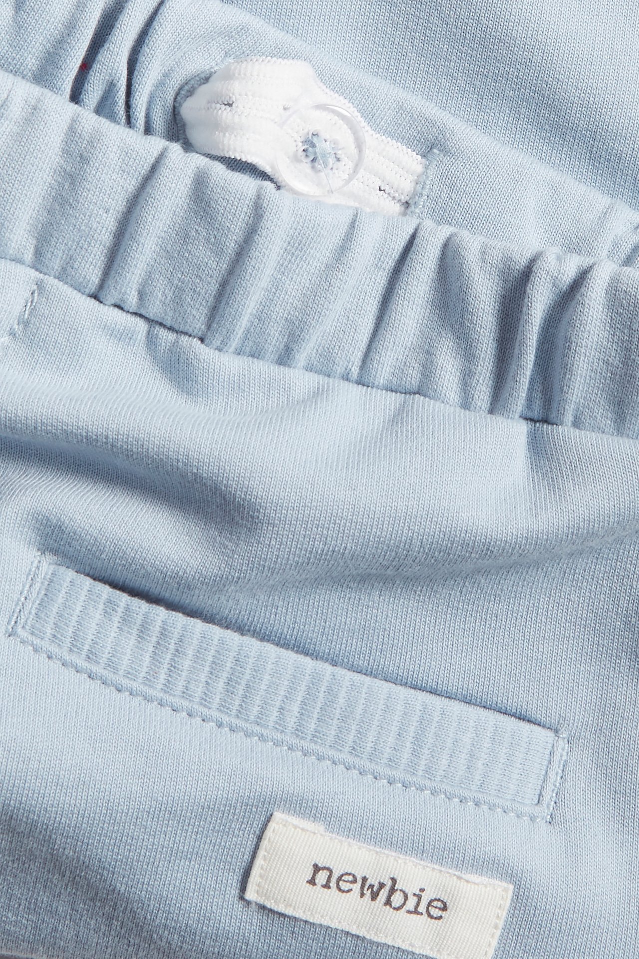 Close-up of light blue cotton jogging bottoms with elasticated waist, white drawstring, button, and front pocket.