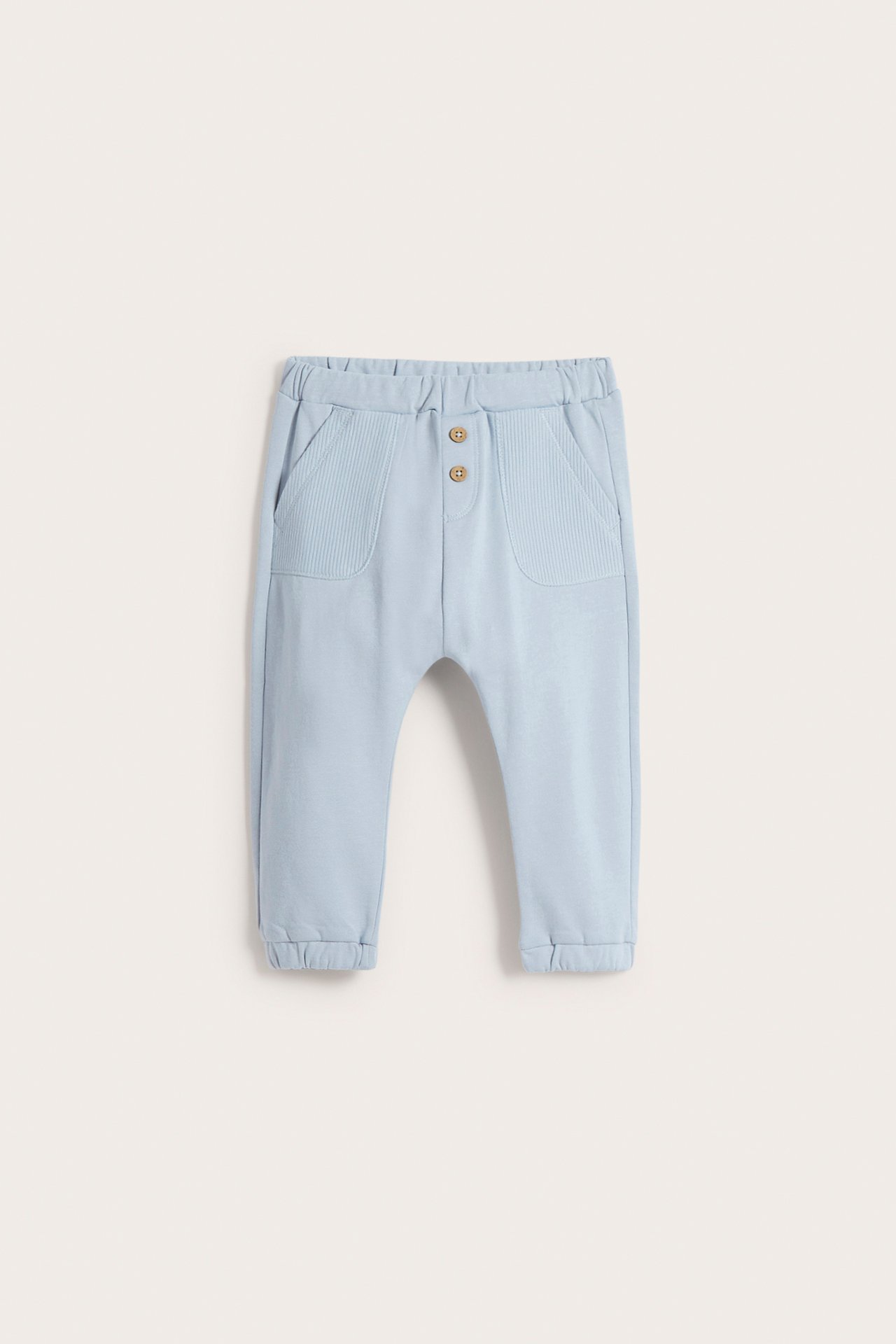 Front view of light blue baby cotton jogging pants with elasticated waist, two buttons, and ribbed front pockets.