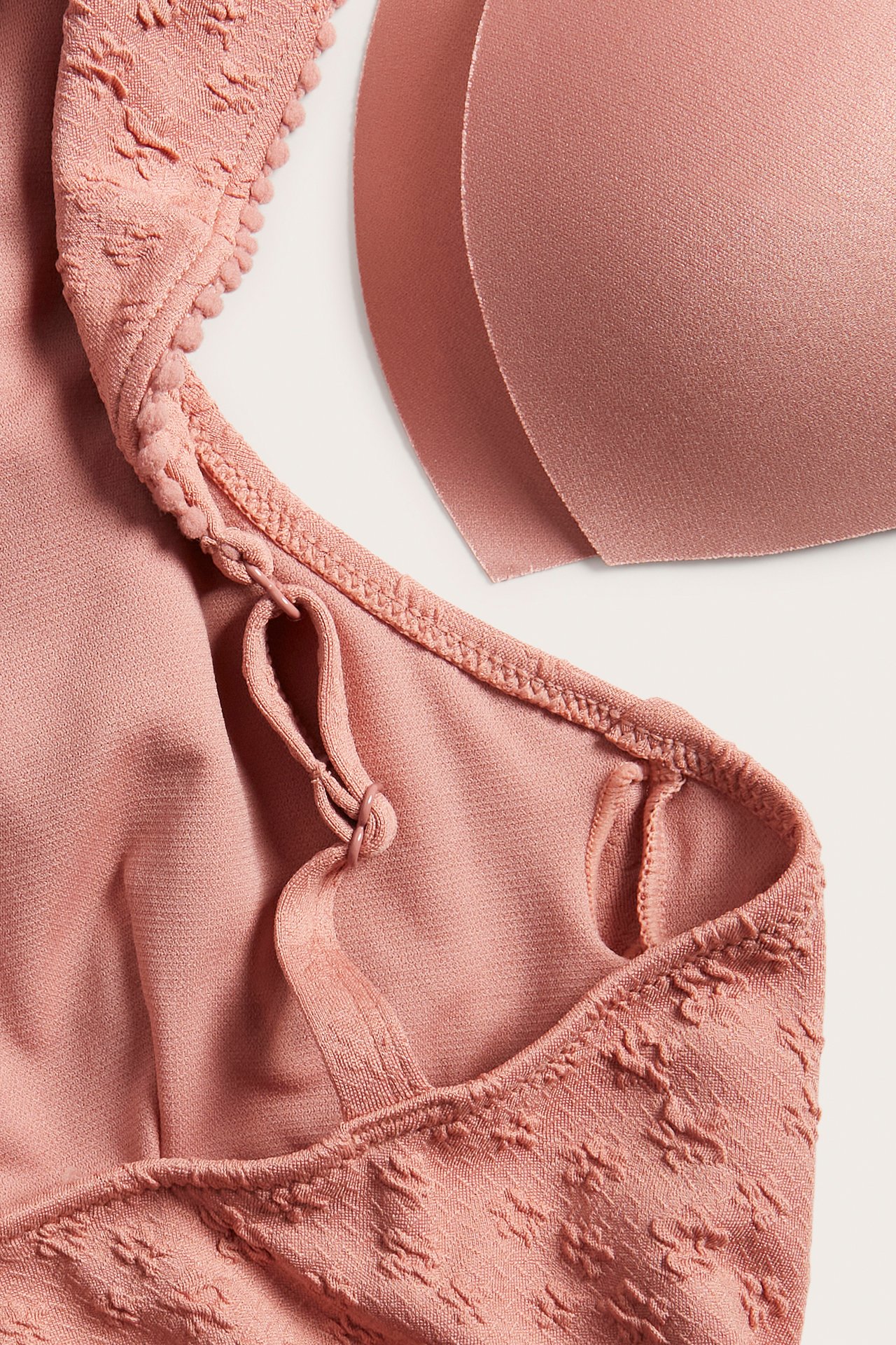 Nahaufnahme eines rosa Badeanzugs mit Jacquard-Blumen, Pompon-Borte, verstellbarem Träger und zwei herausnehmbaren Polstern.