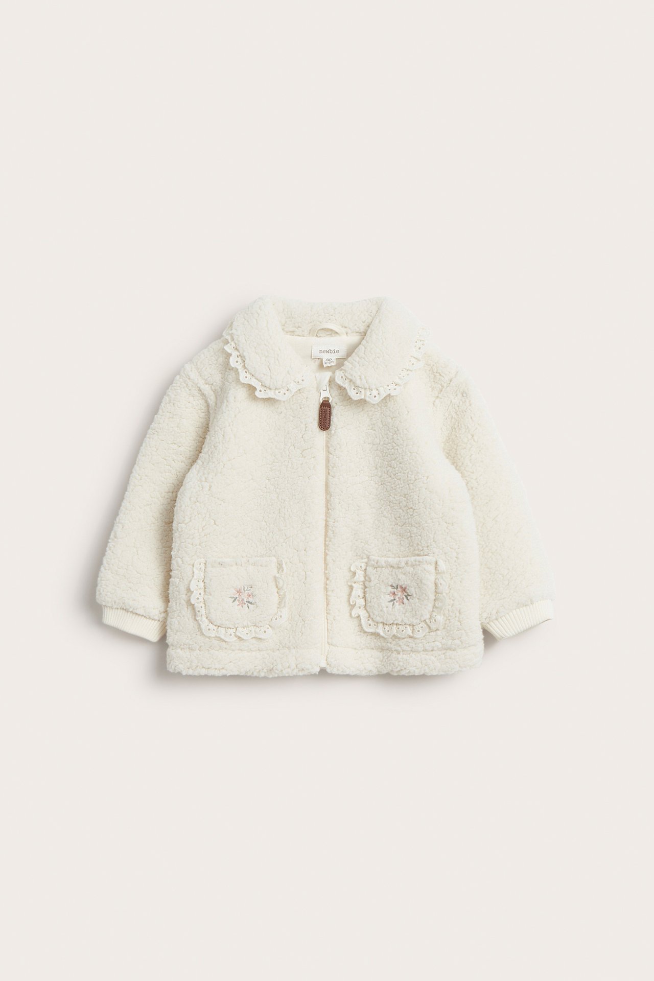Vorderansicht einer cremefarbenen Kinder-Pilejacke mit Reißverschluss, Spitzenkragen und bestickten Taschen.