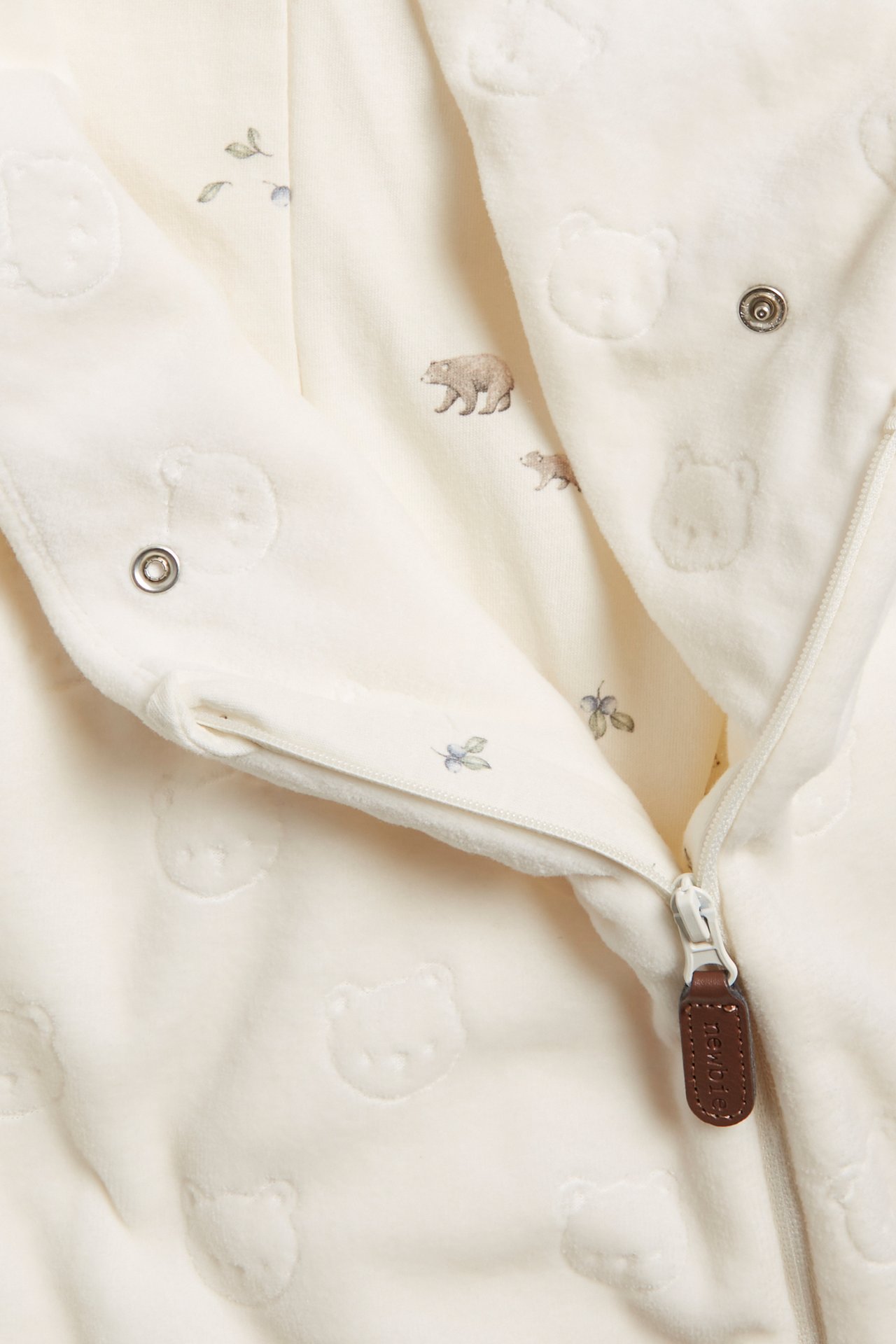 Close-up of an offwhite velour baby coverall with embossed bear pattern and printed lining, diagonal zipper.